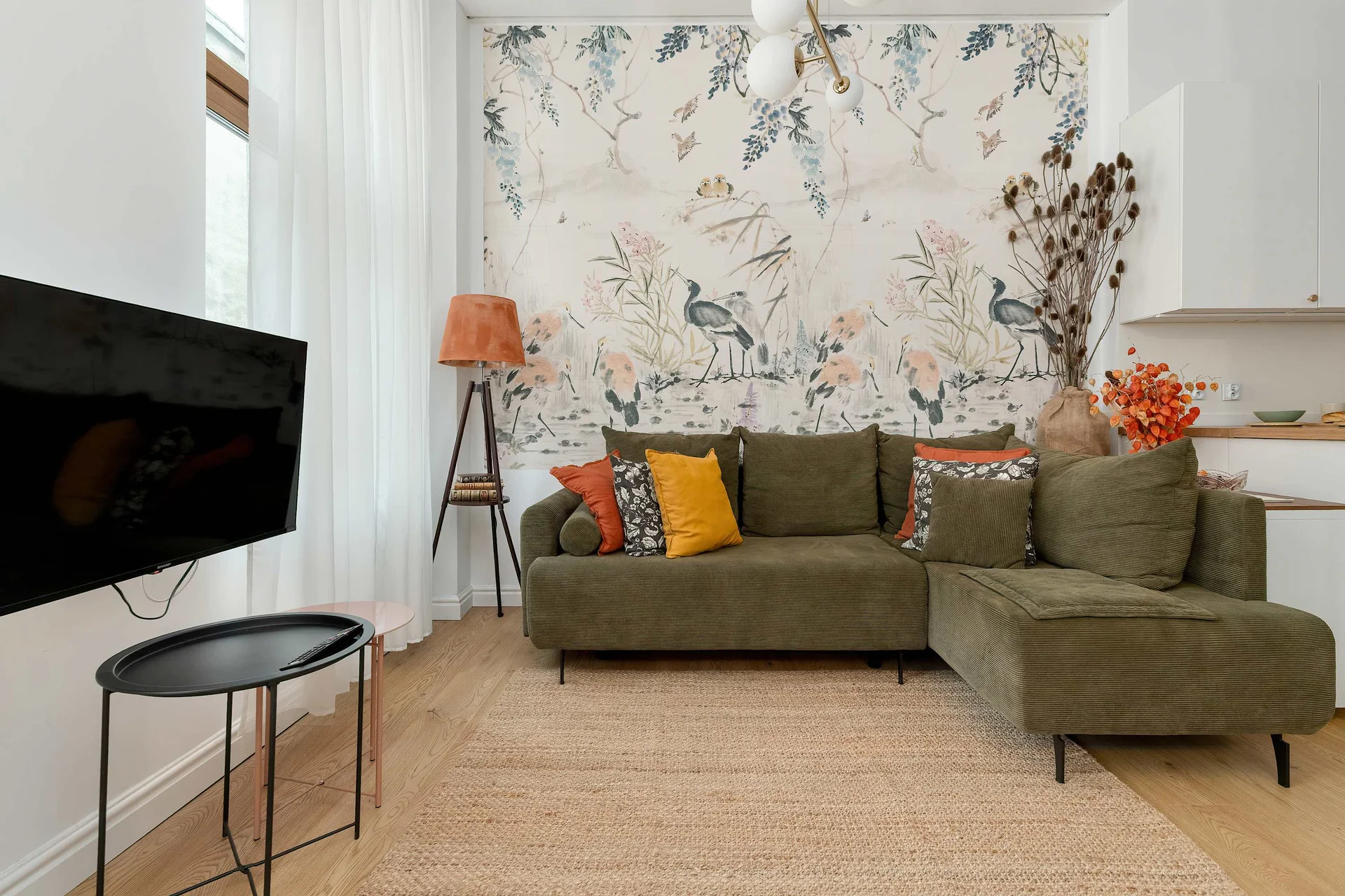1. A cozy living room with an olive-green corner sofa, mustard and patterned cushions, and botanical wallpaper that adds character to the interior.