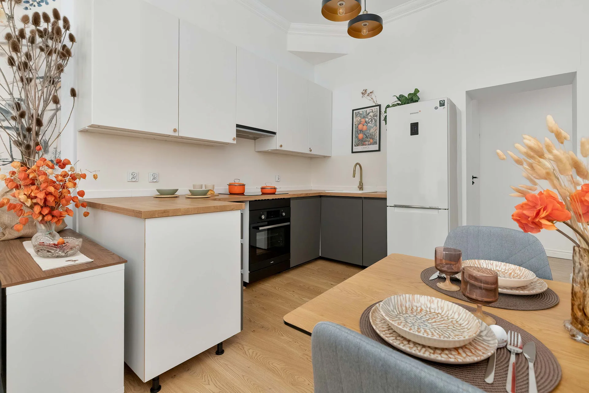 A modern kitchen with white upper cabinets, dark lower cupboards, and a wooden countertop complemented by warm decorative accents.