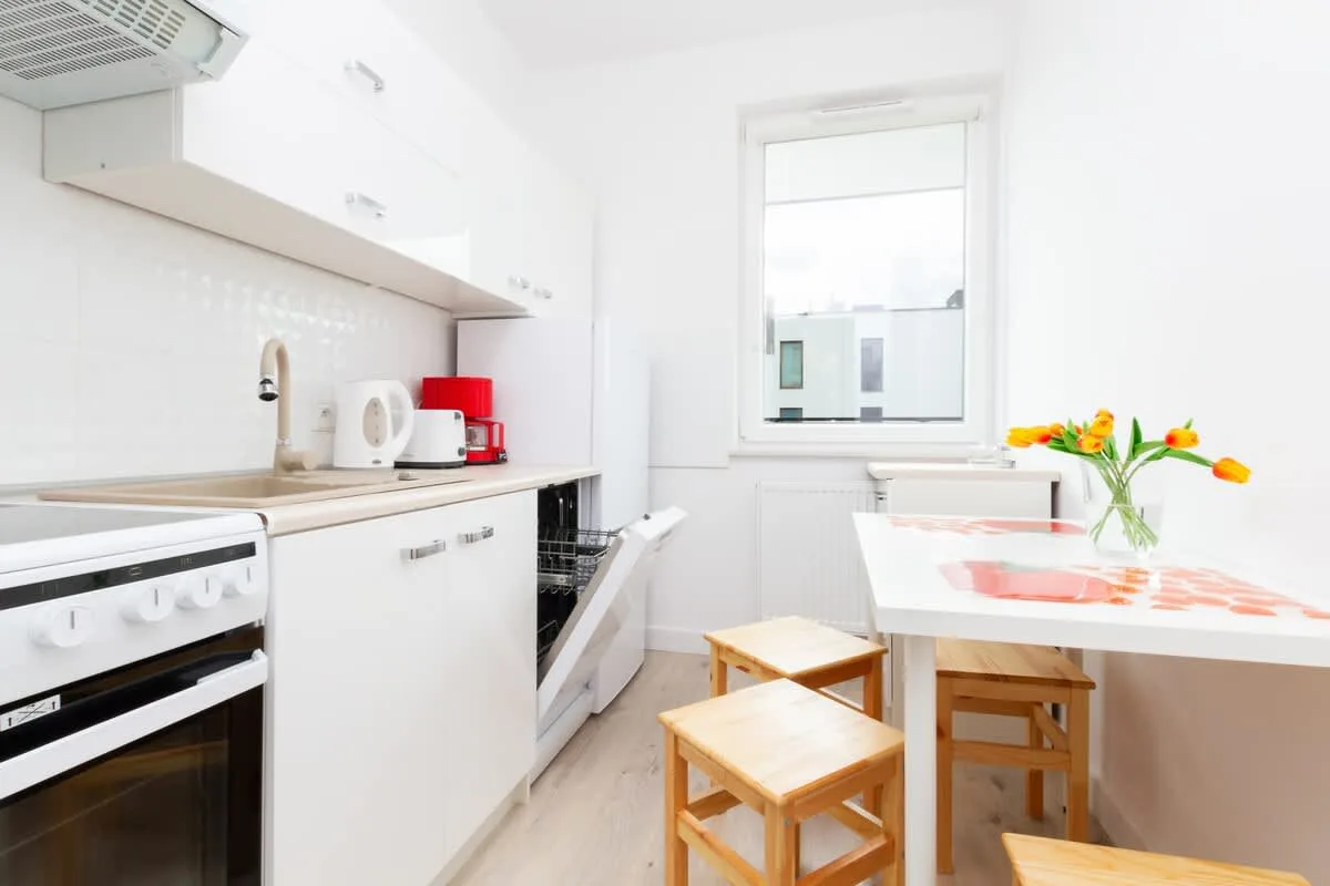 A well-equipped kitchen with white cabinets, a stovetop, and a dishwasher. A small dining table with two chairs sits by the window, adding a cozy touch.