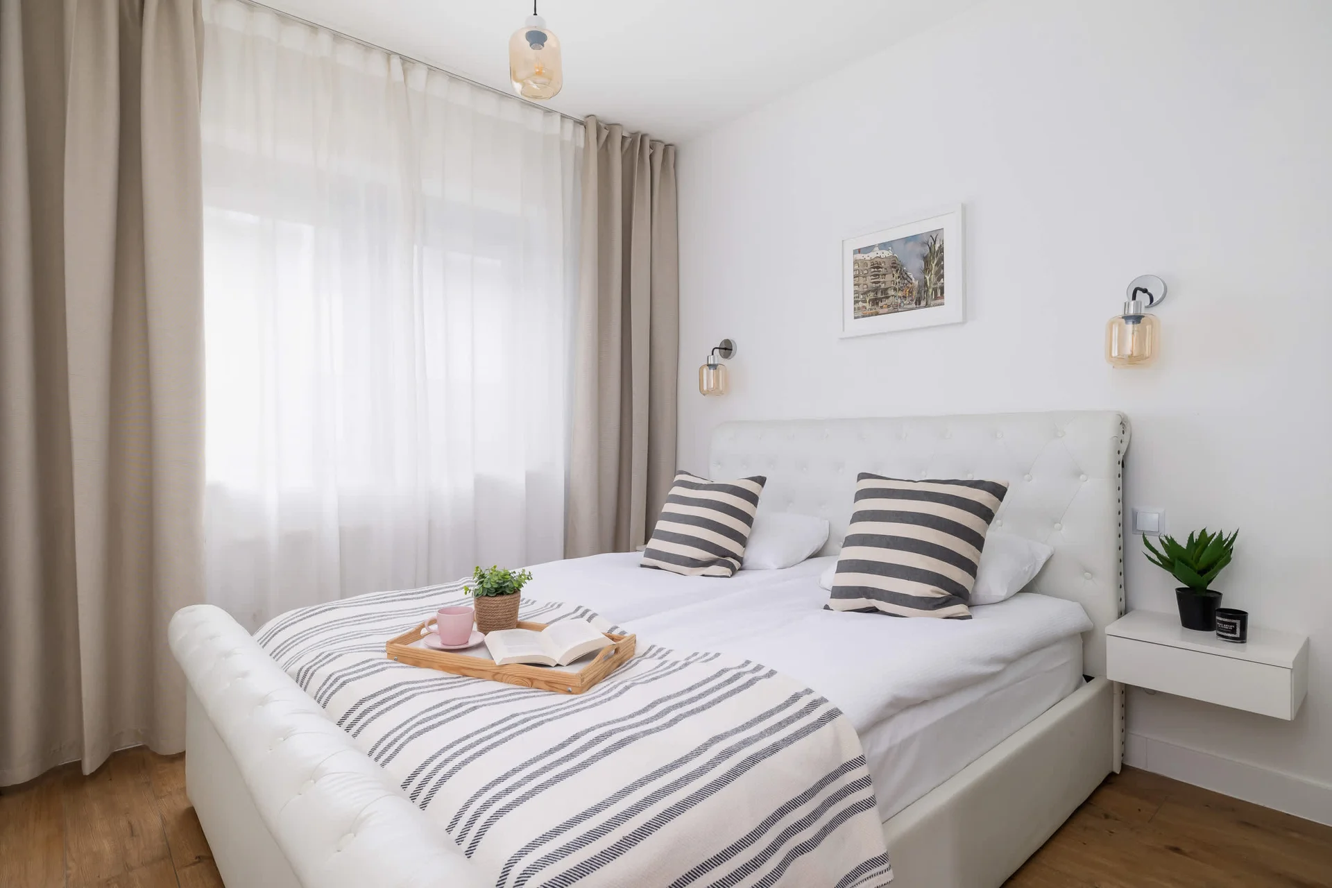A bright and airy bedroom featuring a comfortable bed with striped linens, minimalist decor, and large windows that let in natural light.