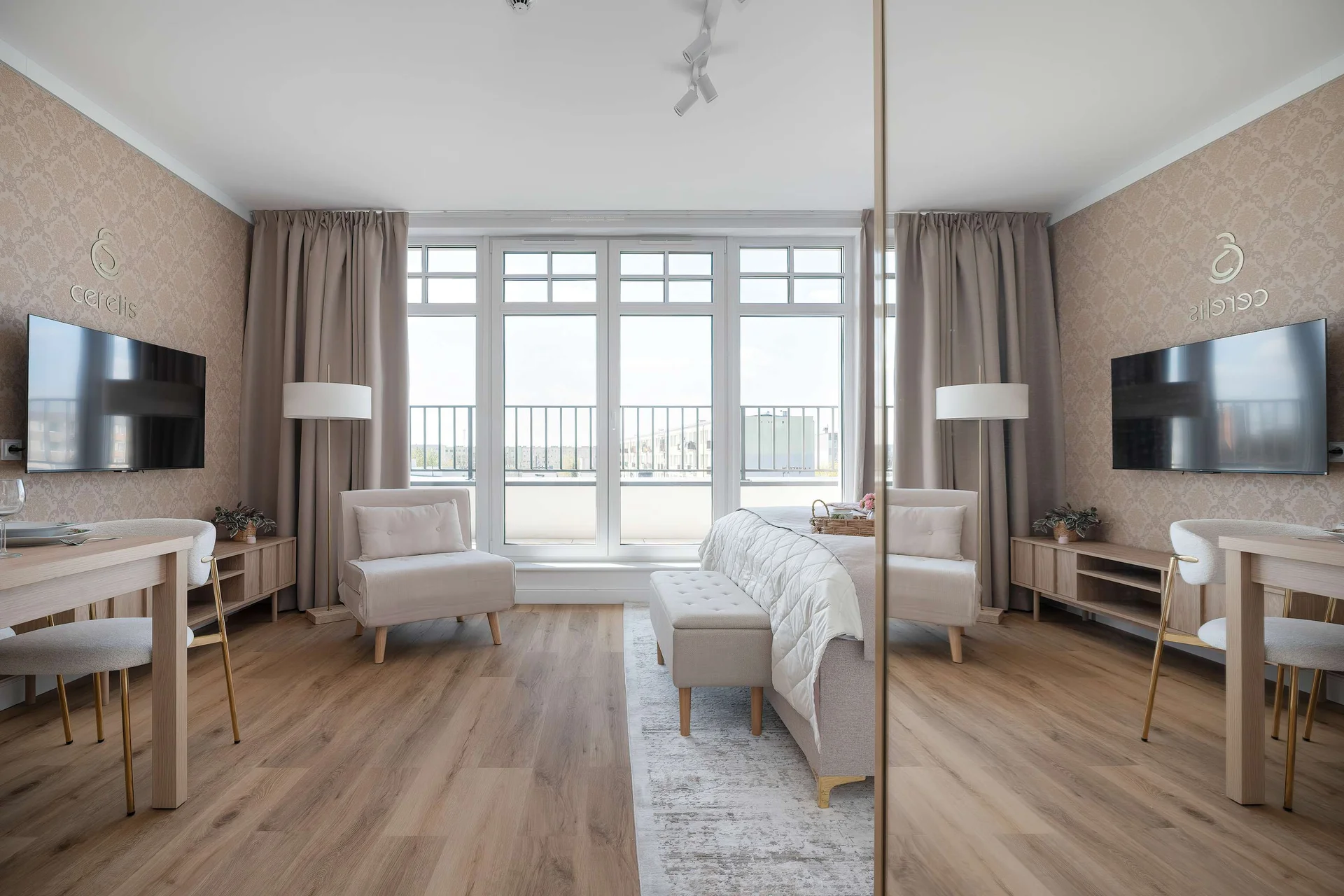 A modern apartment interior with a sleeping area, desk, and large windows brightening the space. Wooden floors and neutral furniture give the room a stylish and welcoming look.