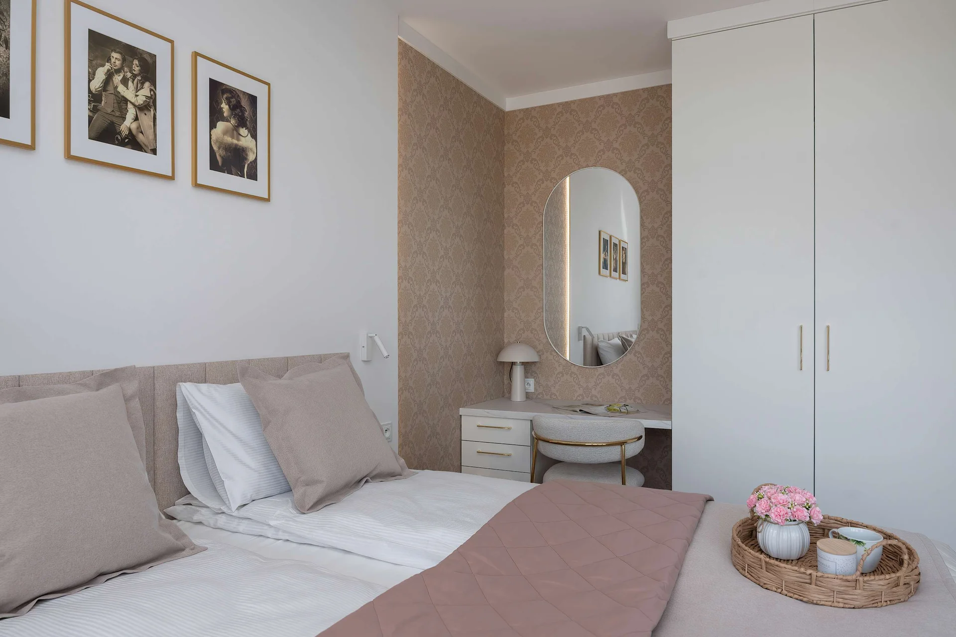 A cozy bedroom with soft beige tones, a neatly made bed, and a small vanity table with a mirror. Minimal decorations and warm lighting create a calm atmosphere.