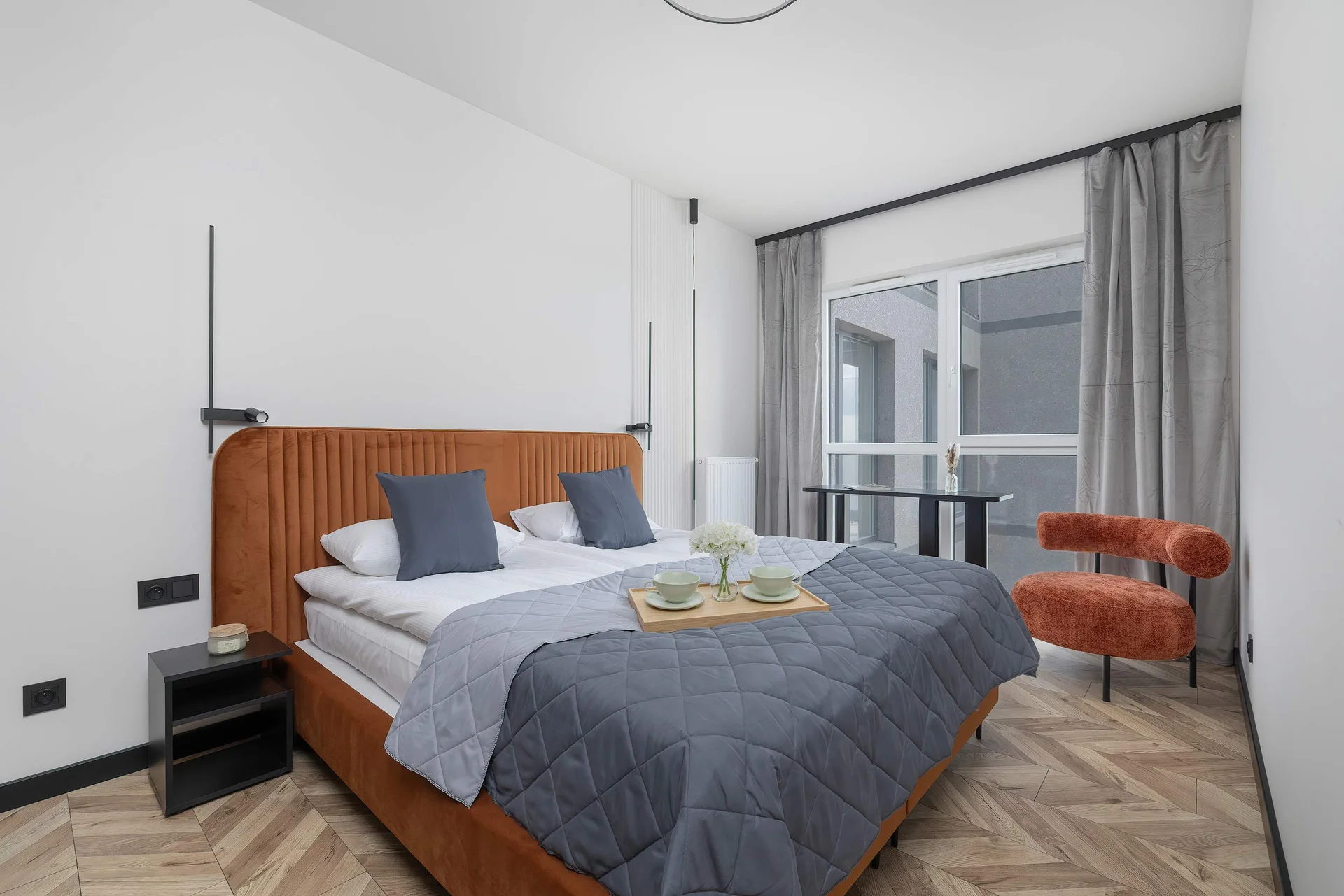 A stylish bedroom featuring a double bed with blue bedding, wooden accents, and a bright balcony door.