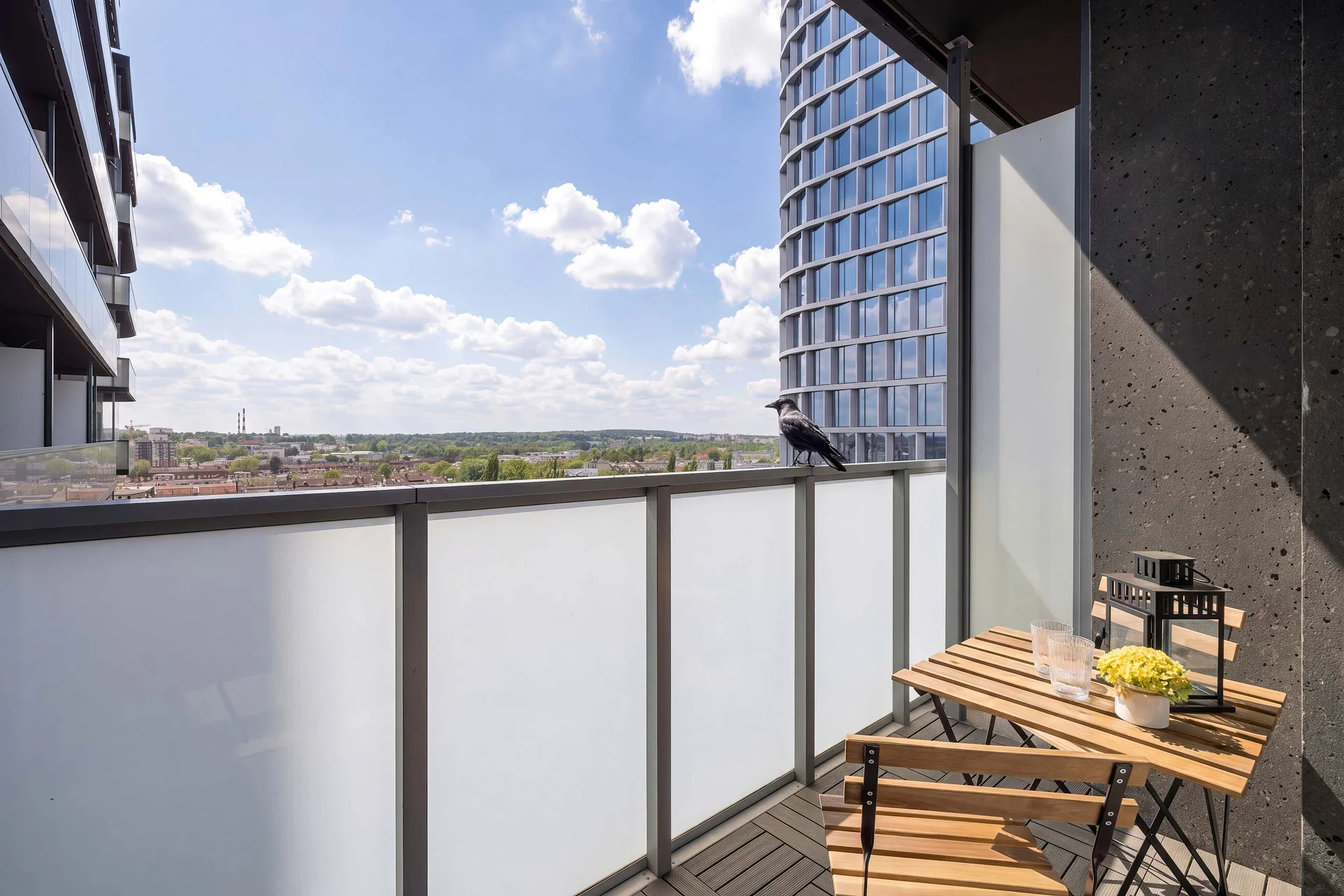 A balcony with outdoor seating overlooking nearby high-rise buildings and the city skyline.