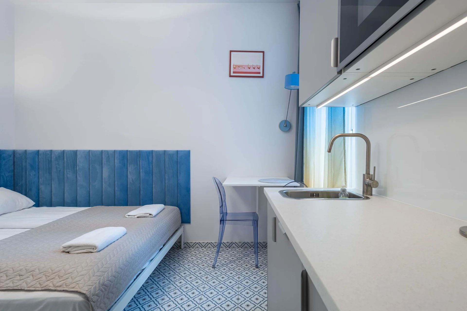 A comfortable bed next to a small kitchenette with a sink.