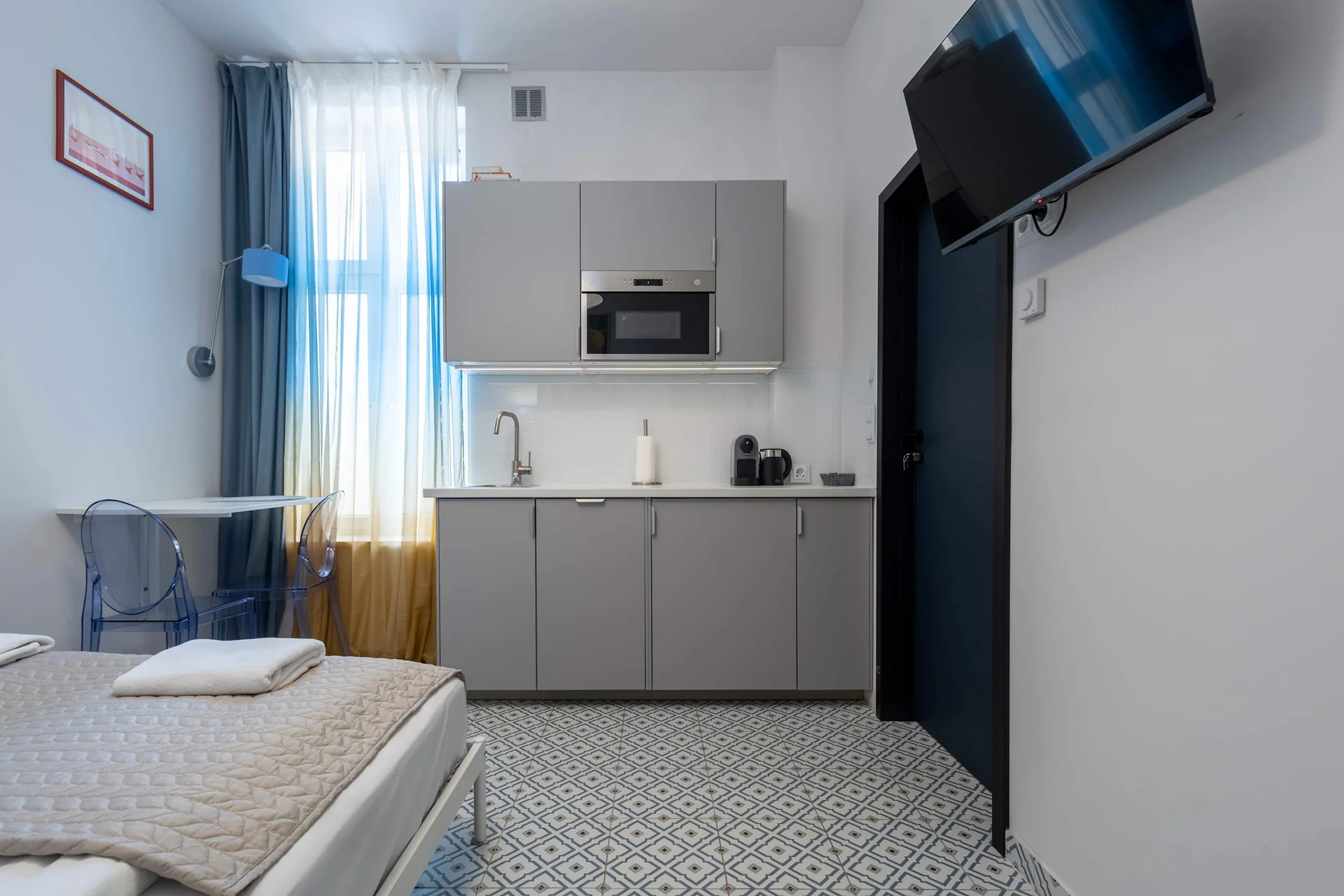 A compact kitchenette with modern cabinets and a window with blue curtains. The space is bright and functional.