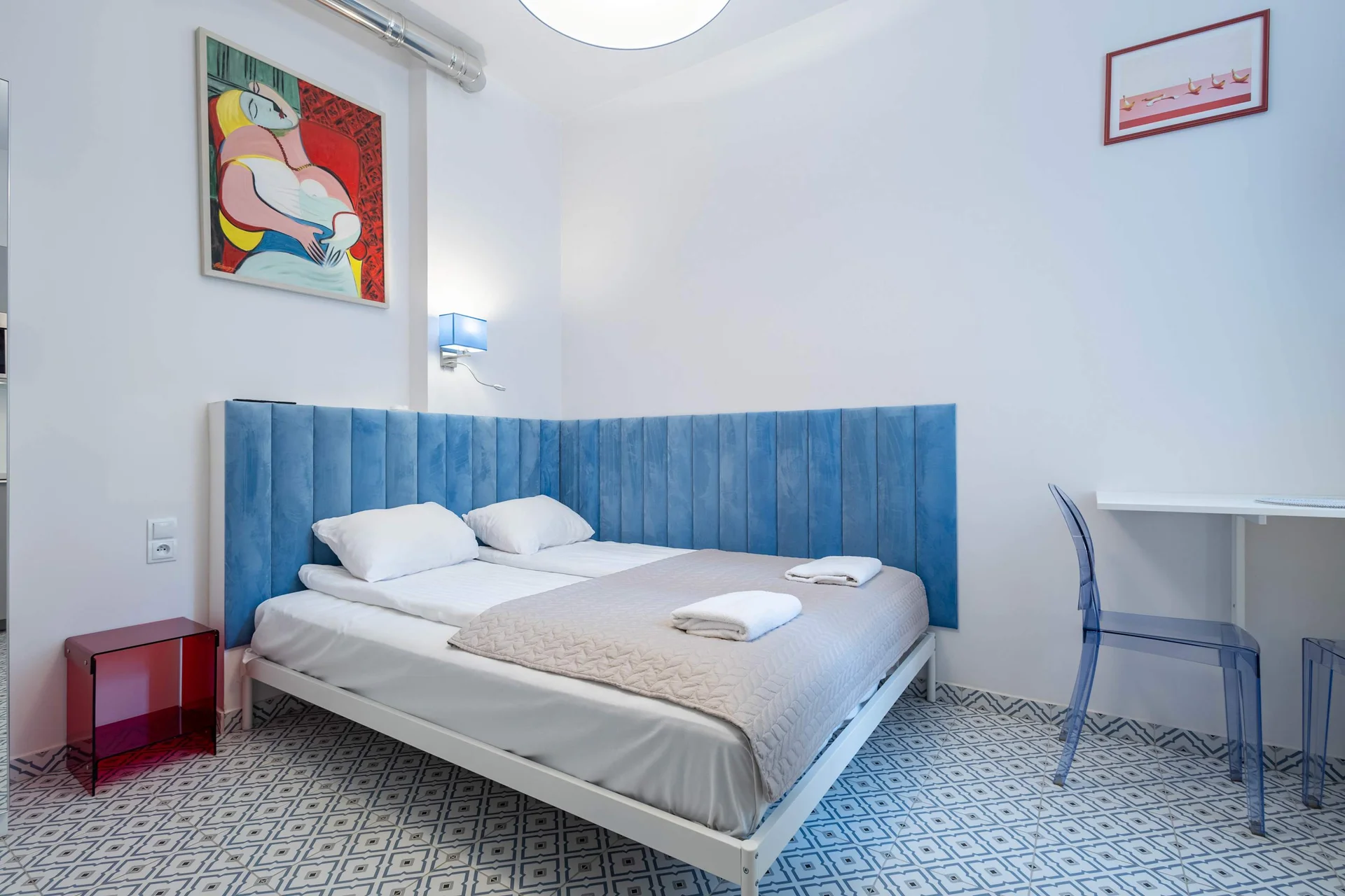 A bright room with a double bed and a small table by the window. The blue accents create a cozy atmosphere.