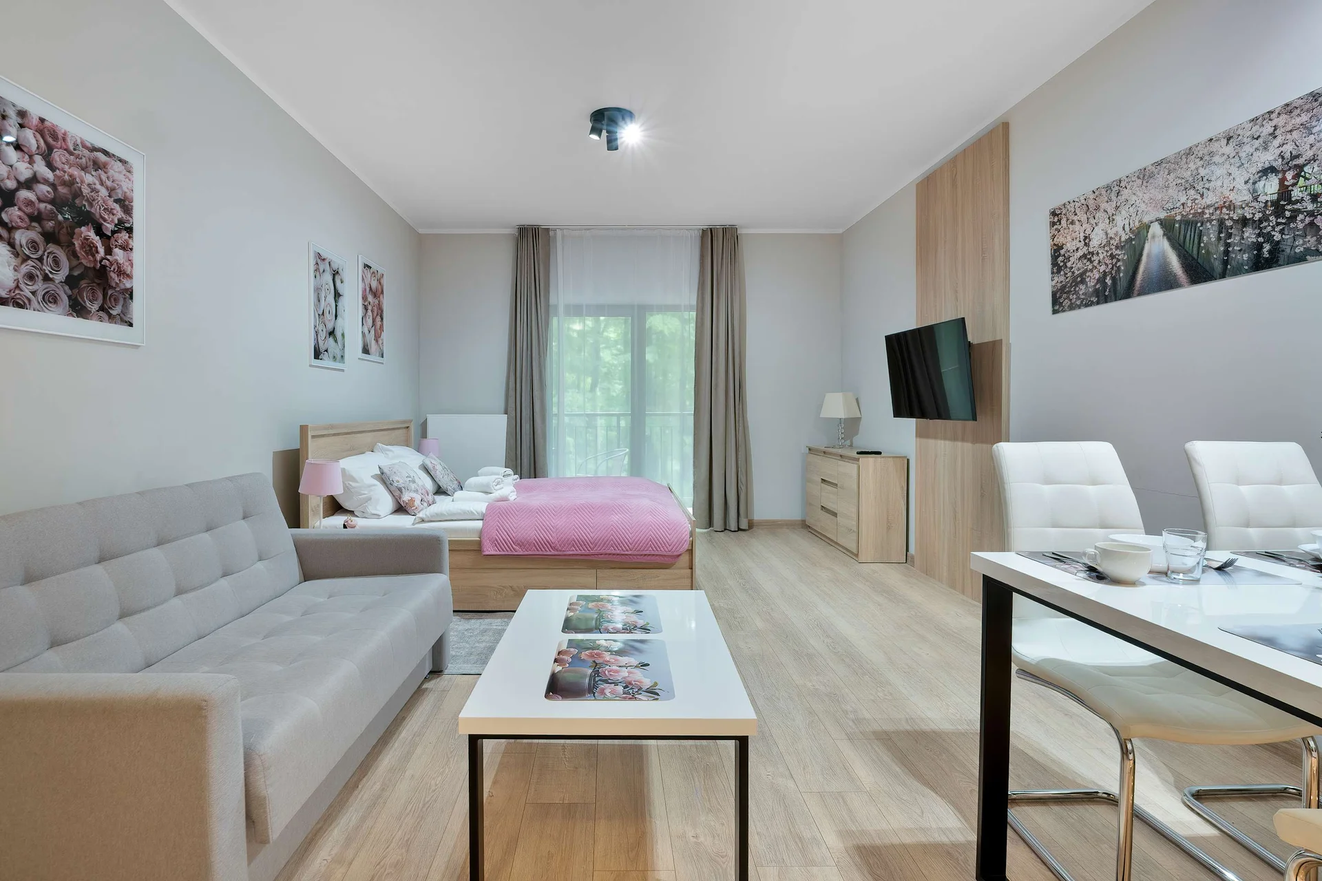 Bright and modern studio apartment with a comfortable sleeping area, seating space, dining table, and access to a private balcony.