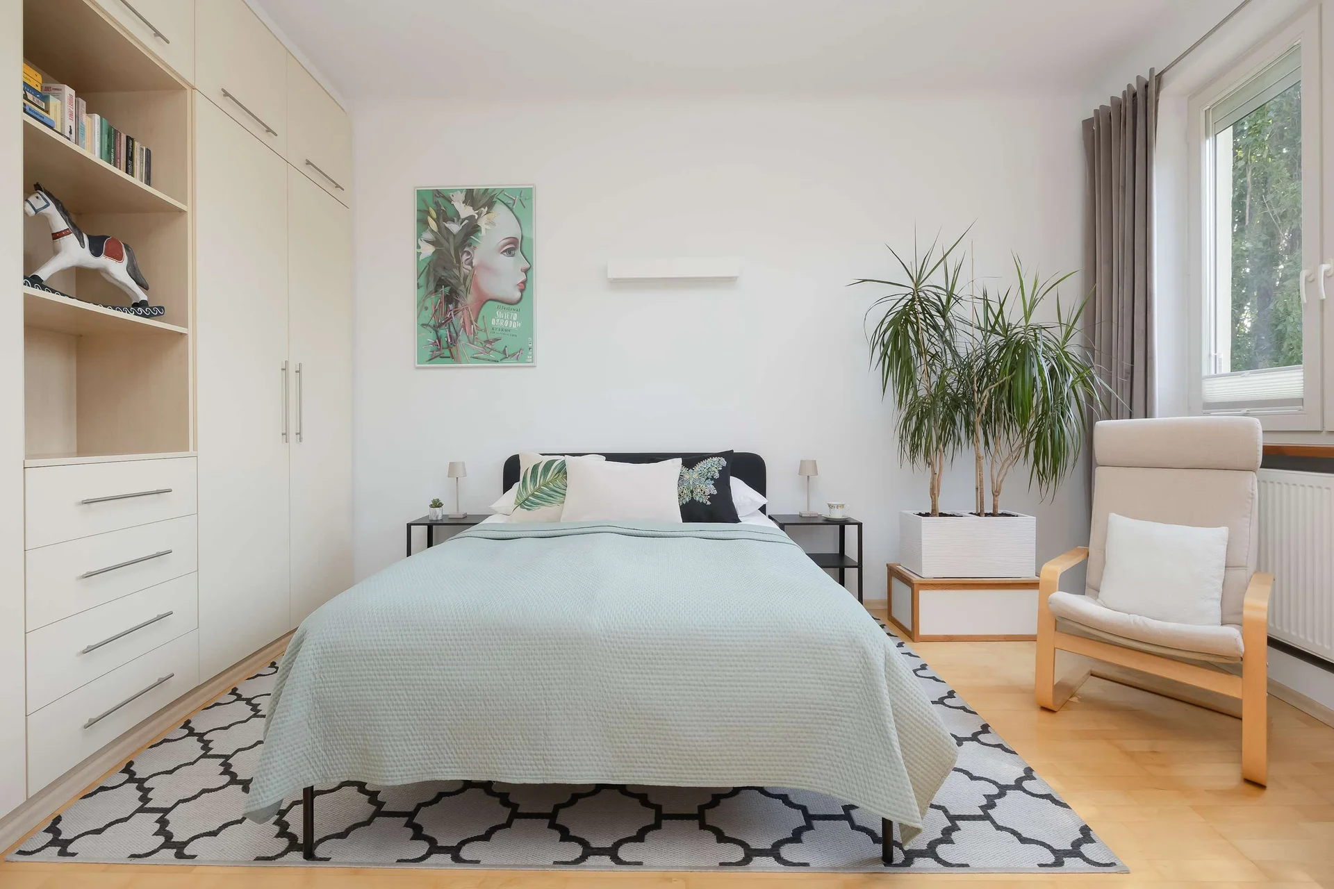 The bedroom area is photographed from the foot of the bed, highlighting the spacious layout and tasteful furnishings. A potted plant adds a fresh decorative touch.