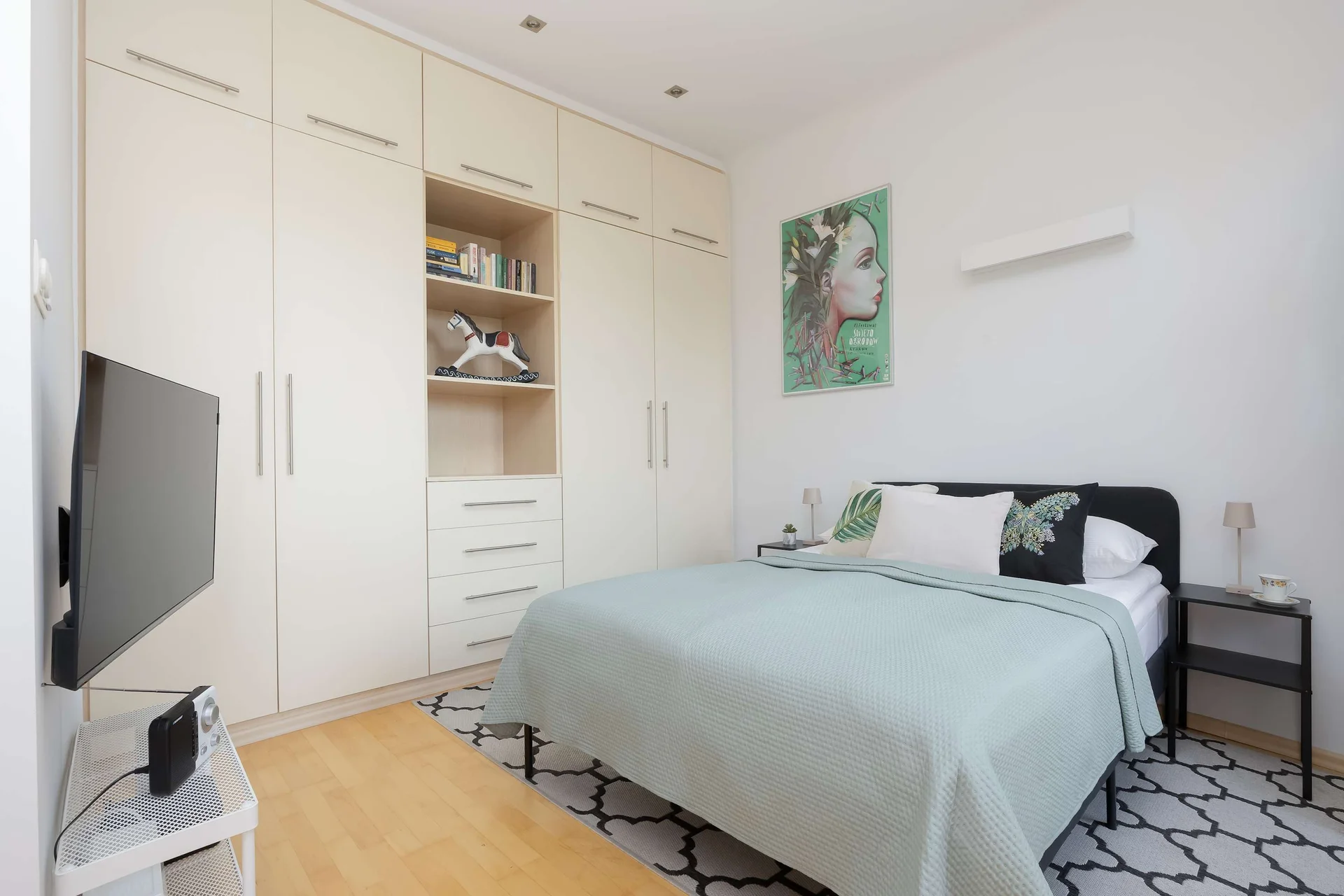 The sleeping area includes a double bed, built-in shelving, and a television opposite the bed. Minimalist décor creates a calm and uncluttered atmosphere.