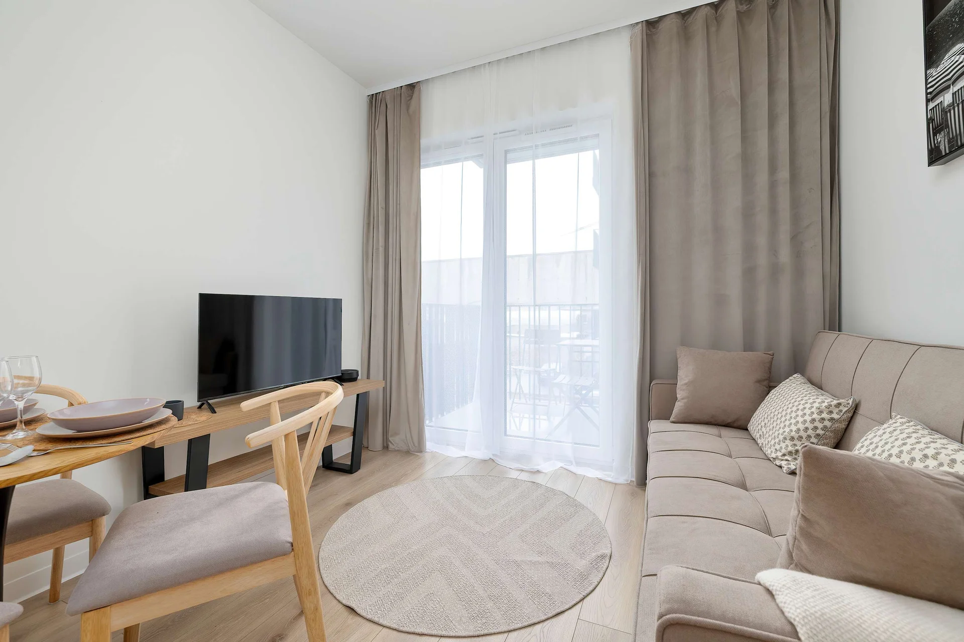Bright living room with a comfortable sofa, TV, dining table, and large windows overlooking the balcony.