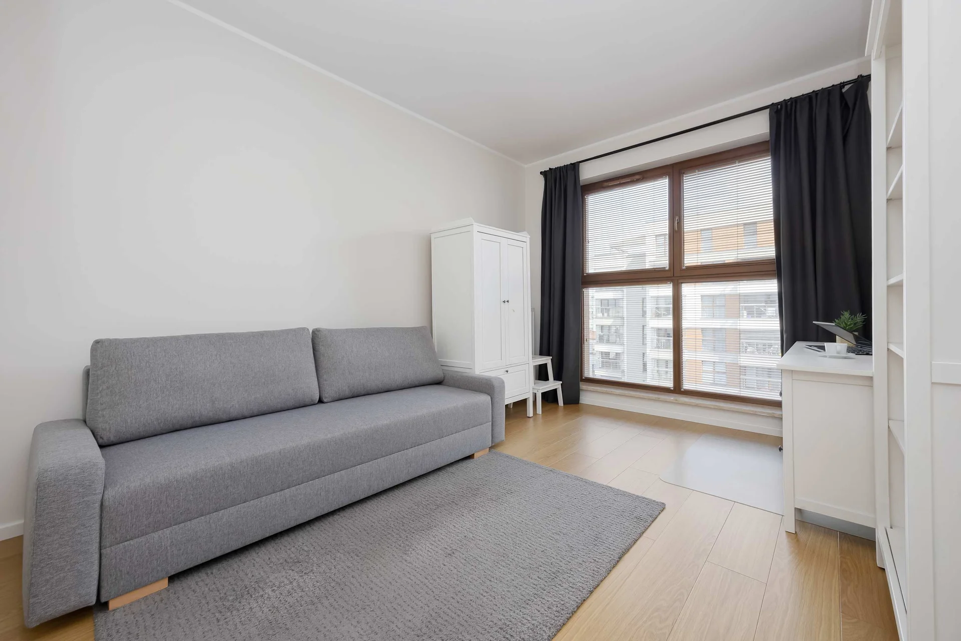 Functional second bedroom with a sofa bed, wardrobe, and a large window providing plenty of natural light.