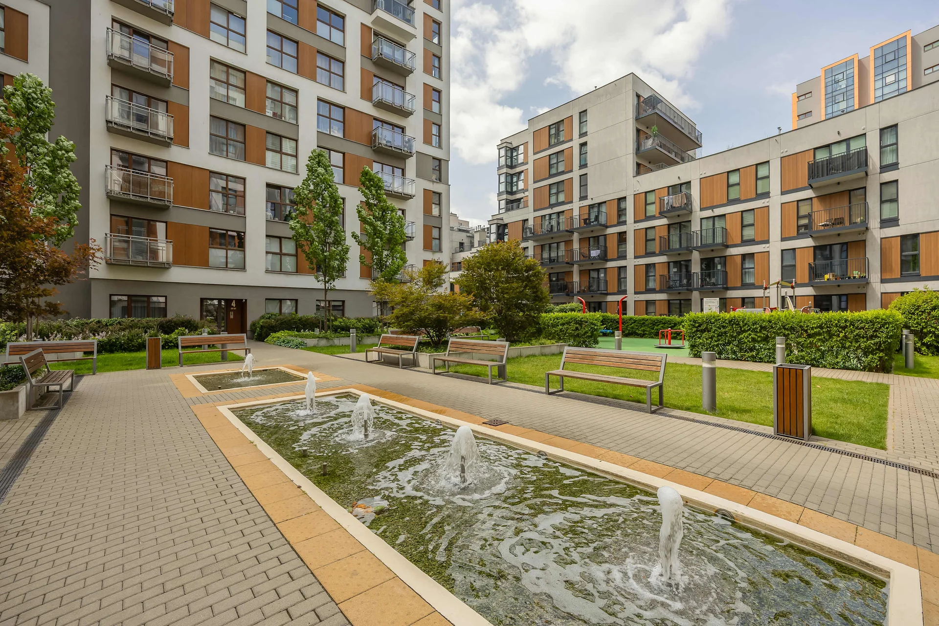 Beautifully landscaped residential courtyard with walking paths, greenery, and a decorative water feature.