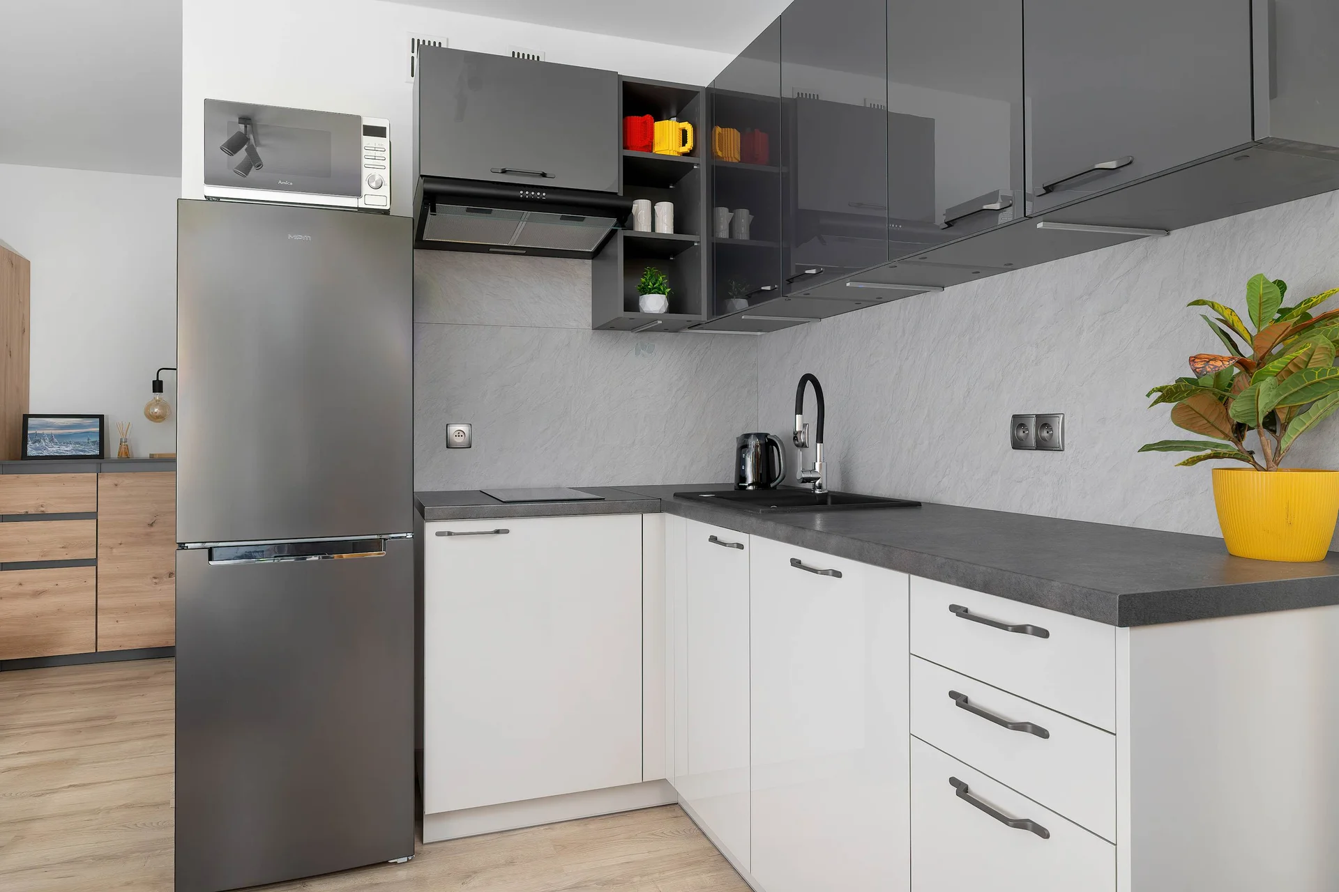 A contemporary kitchenette space showcases sleek dark grey lower cabinetry topped with light wooden countertops. A tall refrigerator stands at the end of the counter line under bright overhead lighting.