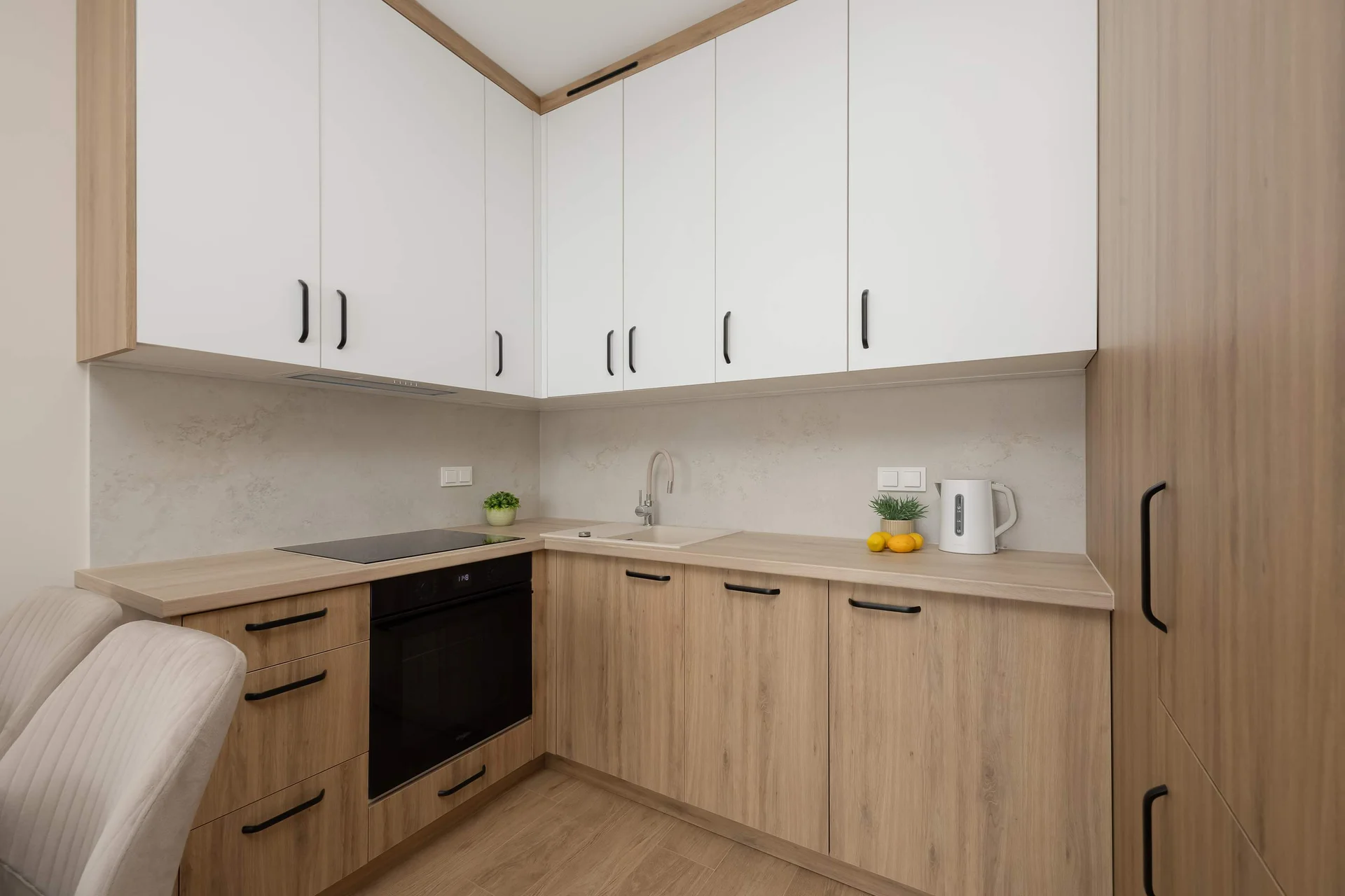 A corner kitchenette combines white upper cabinets with light wood-grained lower units. Built-in appliances include a black induction cooktop and oven.
