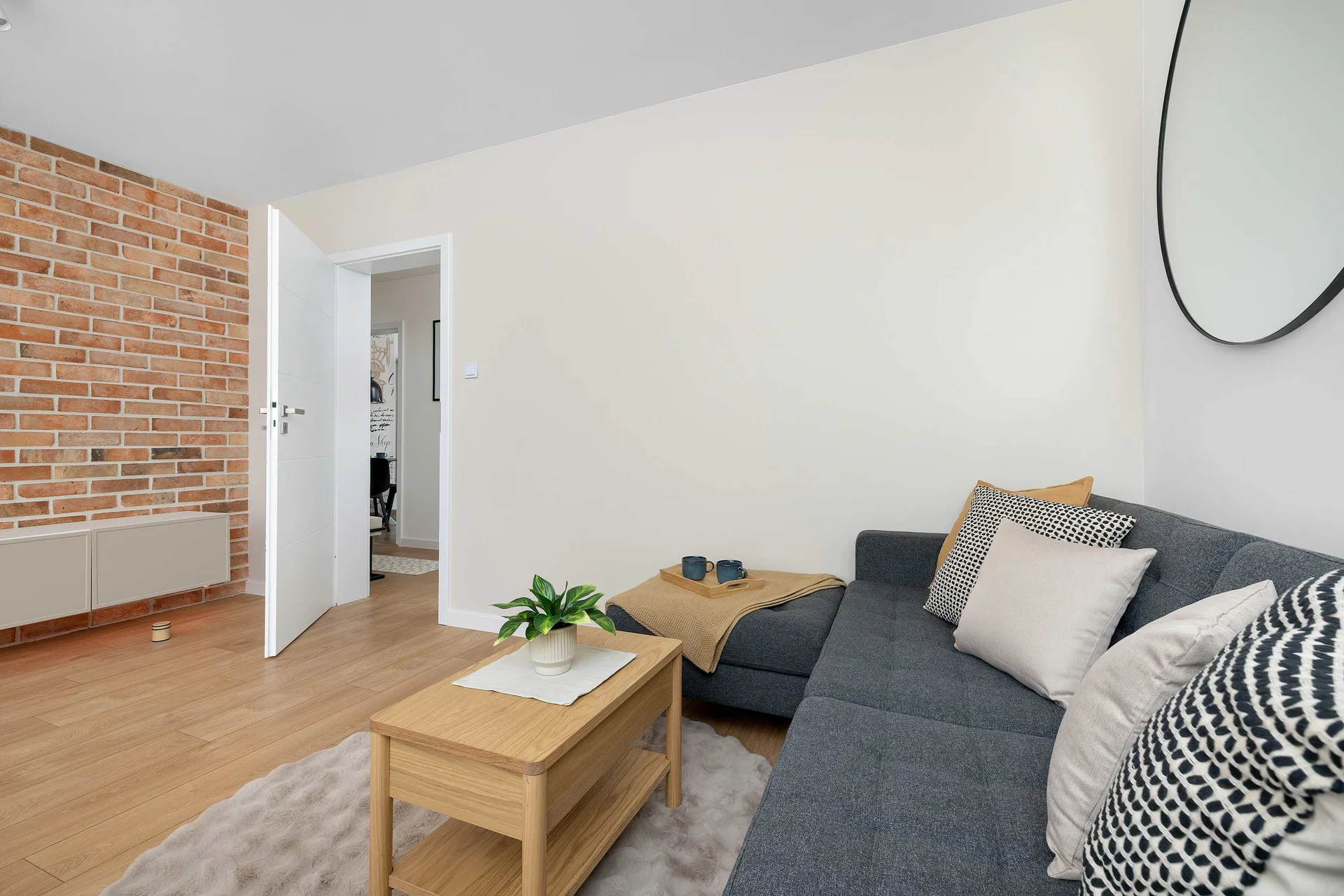 An open-concept living area provides a view into a secondary room through a white doorway. A dark sectional sofa and a matching wooden coffee table offer a comfortable spot for relaxation.