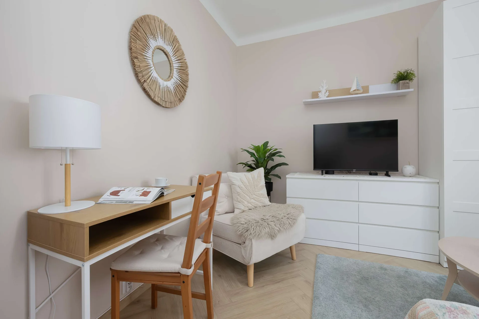 A focused view of the living section highlights the dedicated desk paired with a matching wooden chair. Nearby, a comfortable armchair and a television mounted over white cabinetry create a relaxing environment.