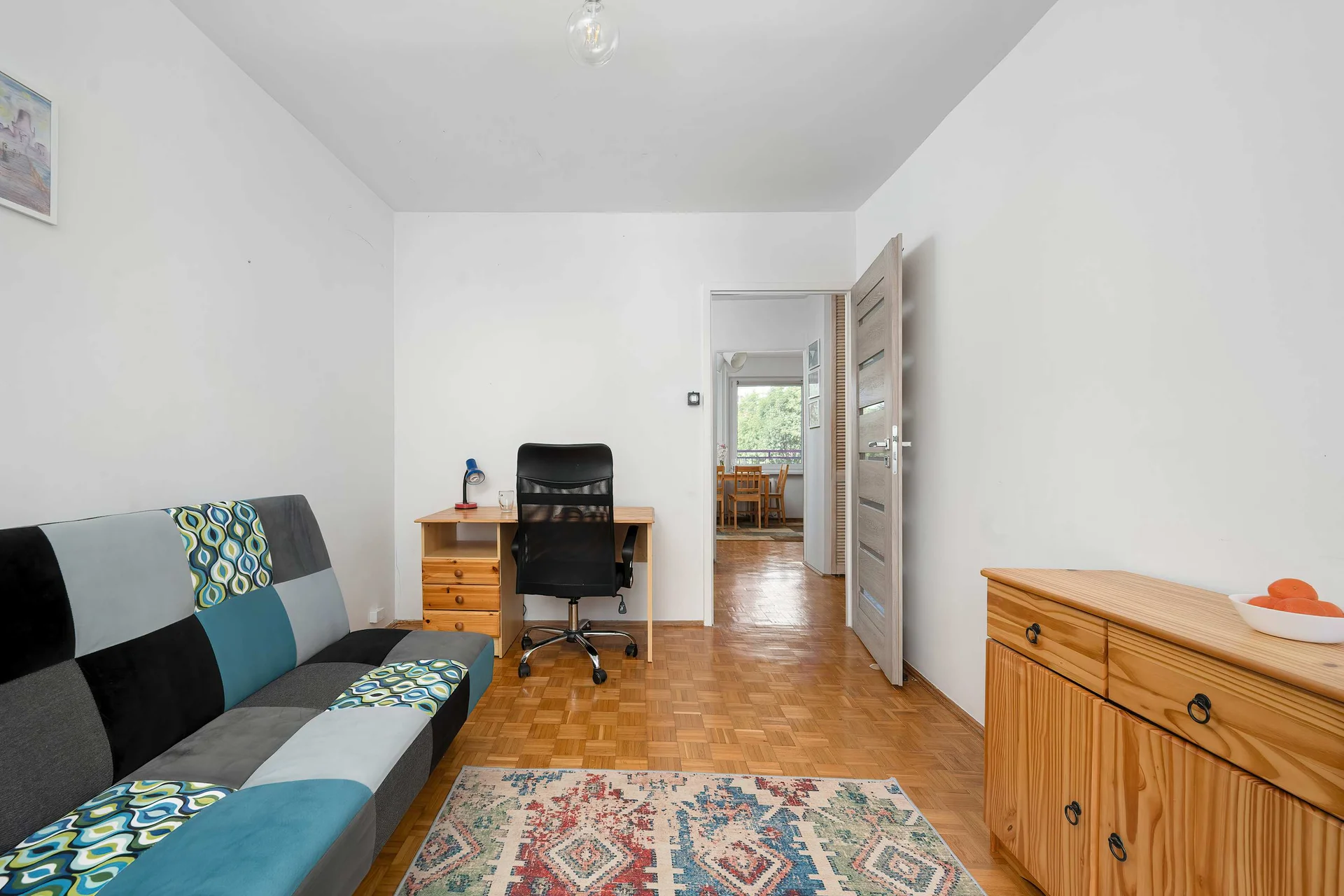 Spacious bedroom with a sofa bed, desk, chest of drawers, and parquet flooring.