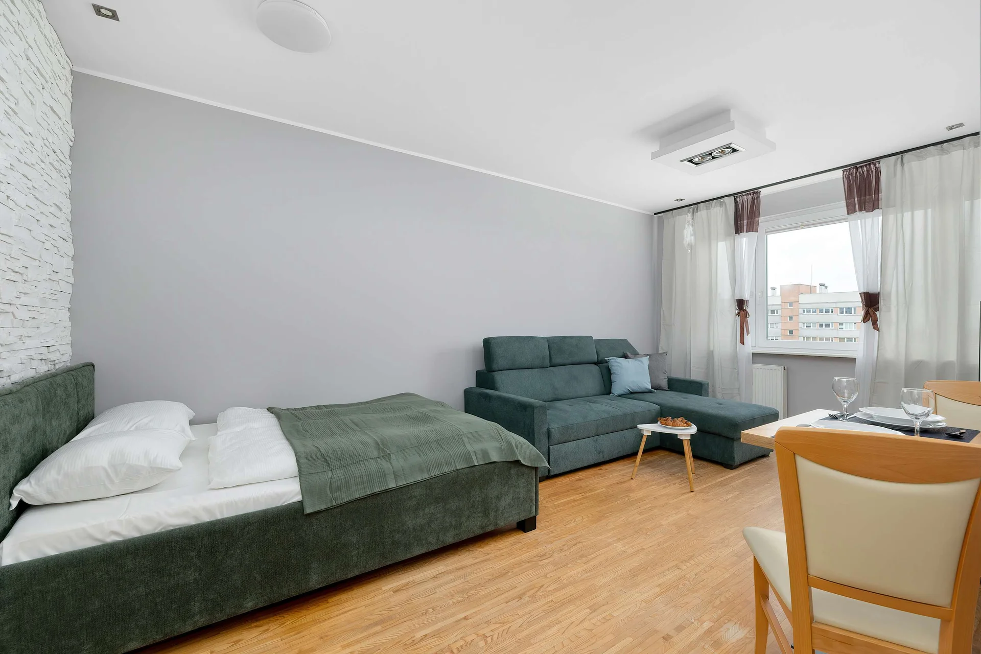 A comfortable room with a double bed, a sofa, and access to a balcony. Large windows provide plenty of natural light.