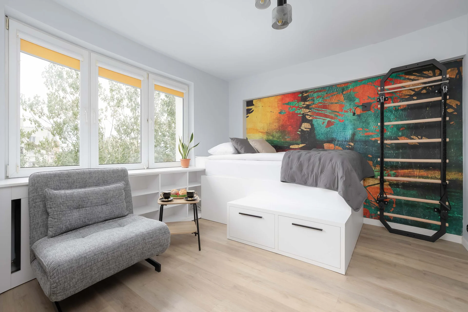 Bright and cozy studio featuring a single bed, a comfortable single sofa bed, a dining area, large windows, and colorful artwork.