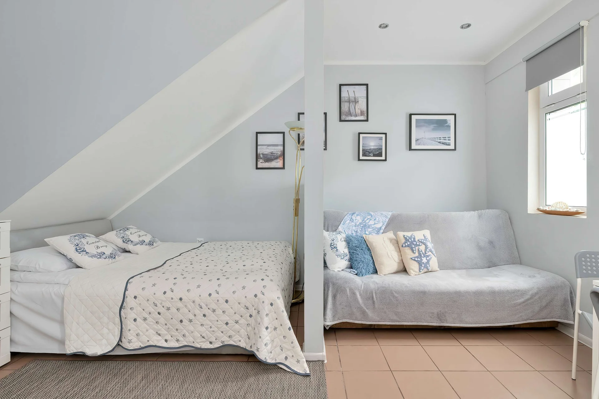 A wide shot of the studio apartment highlights the division between the sleeping area and the seating zone. The bed with its textured white blanket sits on the left, while the grey sofa is visible on the right.