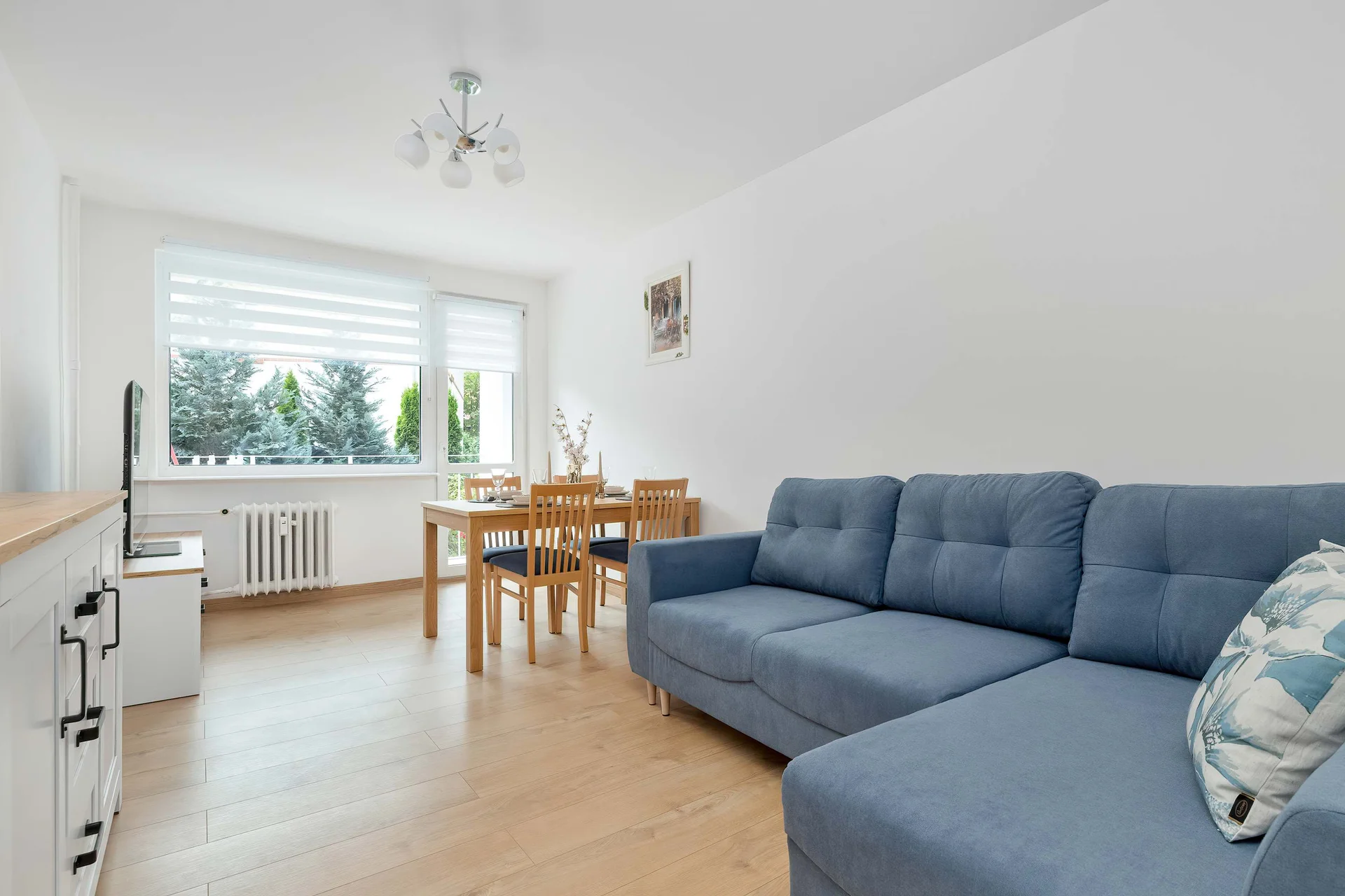 A bright open-plan bedroom combines a comfortable sofa and dining table in one spacious area. Large windows allow plenty of natural light to brighten the interior.