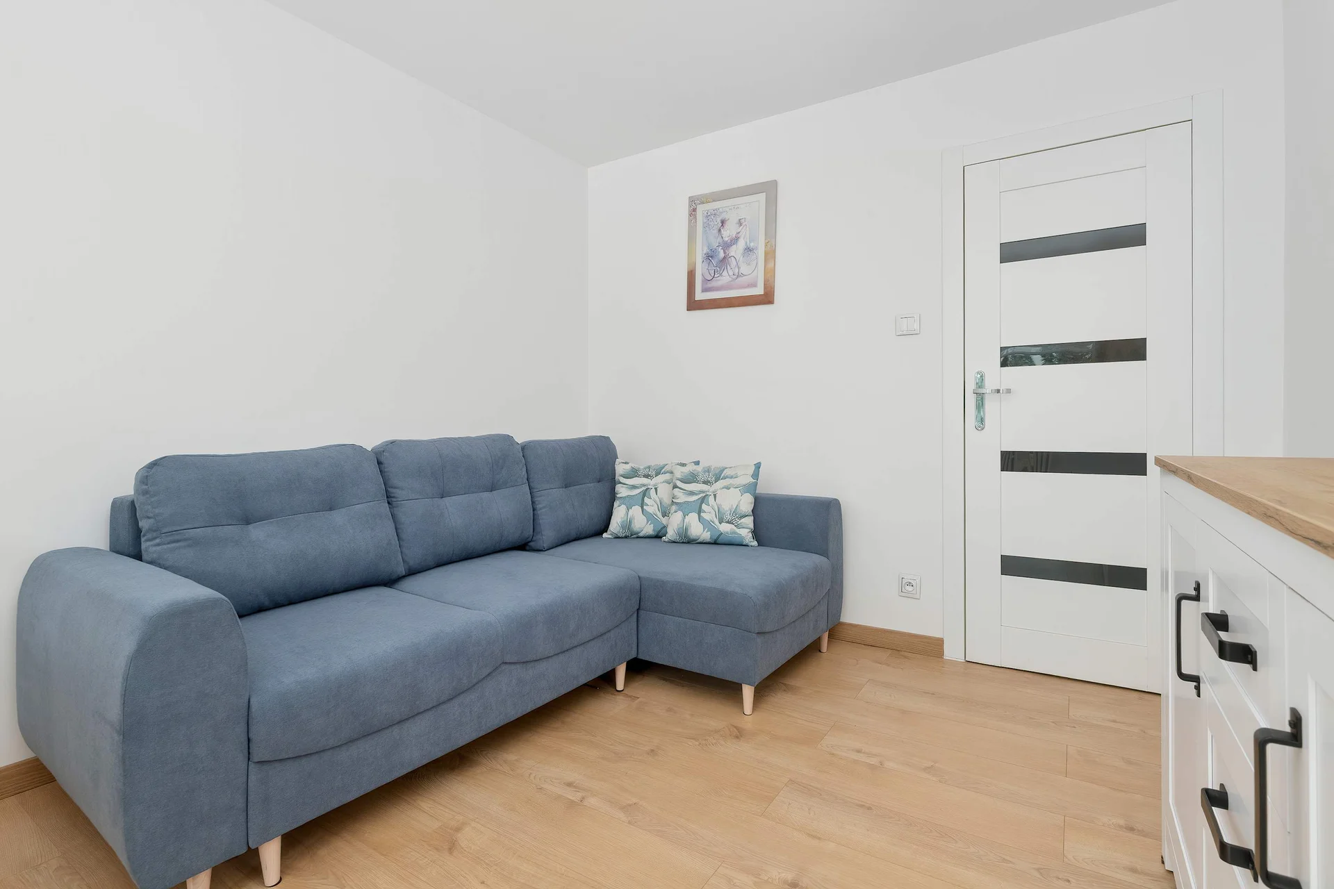 The  bedroom area features a blue sofa facing a television, creating a comfortable space for relaxing. Light wooden flooring enhances the warm atmosphere.