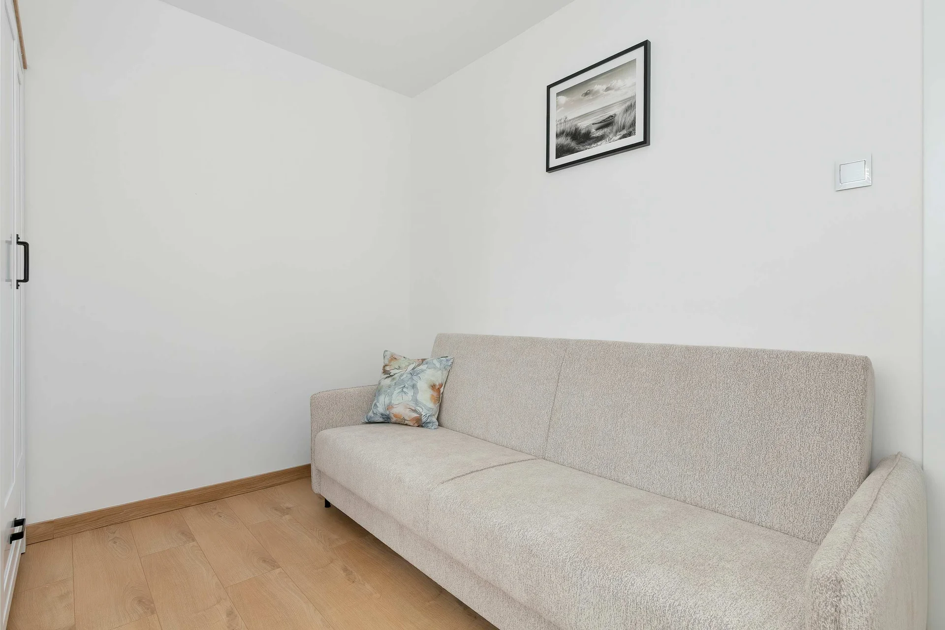 Another cozy bedroom includes a sofa bed against a white wall with simple, minimalist décor. The uncluttered layout creates a calm and functional retreat.