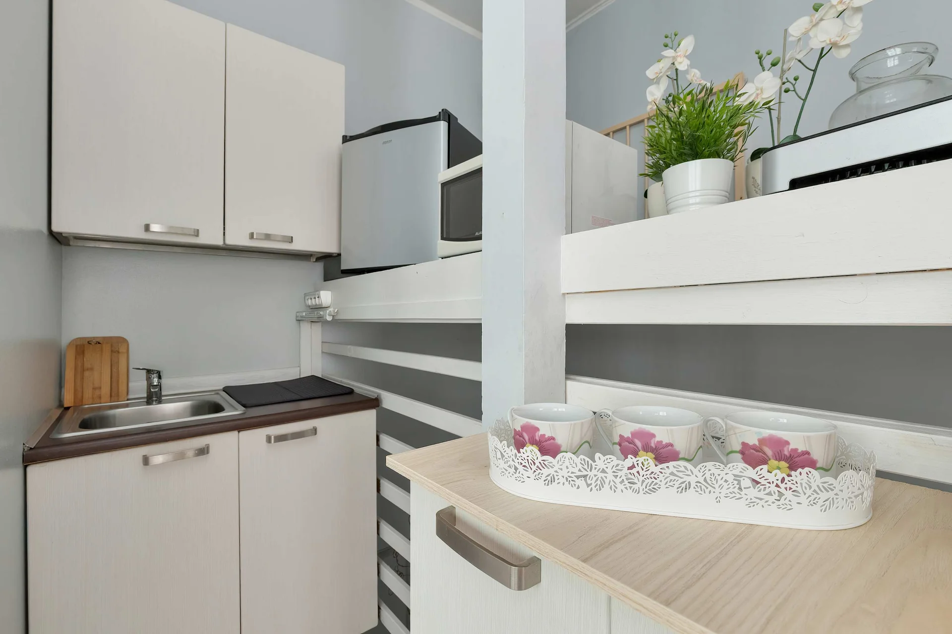 A compact kitchenette equipped with white cabinetry, a microwave, and basic kitchen essentials on the counter. A small shelf unit provides additional storage for organized living.