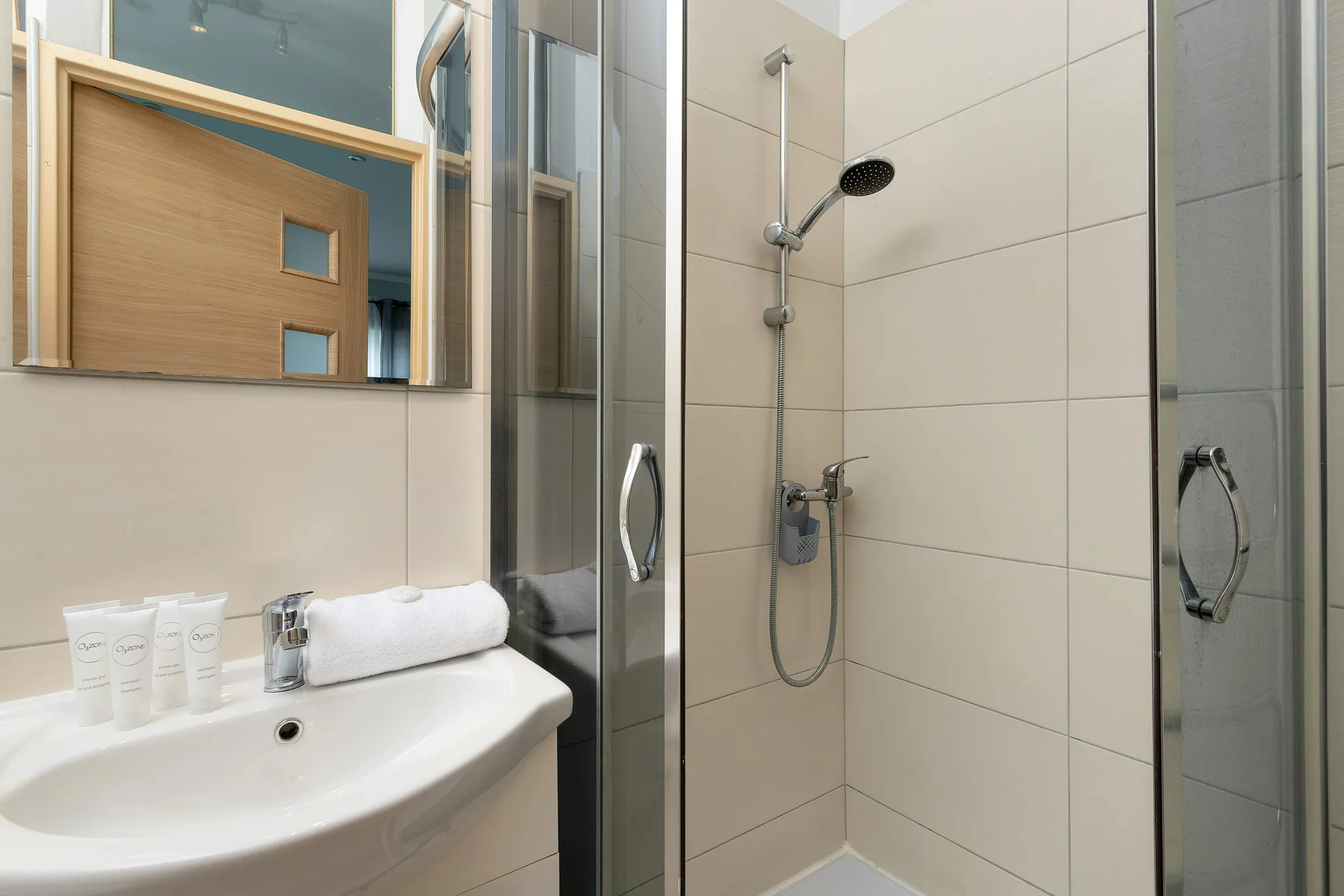 A modern bathroom featuring a walk-in shower with light-colored tiles and a sleek sink. A mirror is mounted above the vanity, enhancing the sense of space.