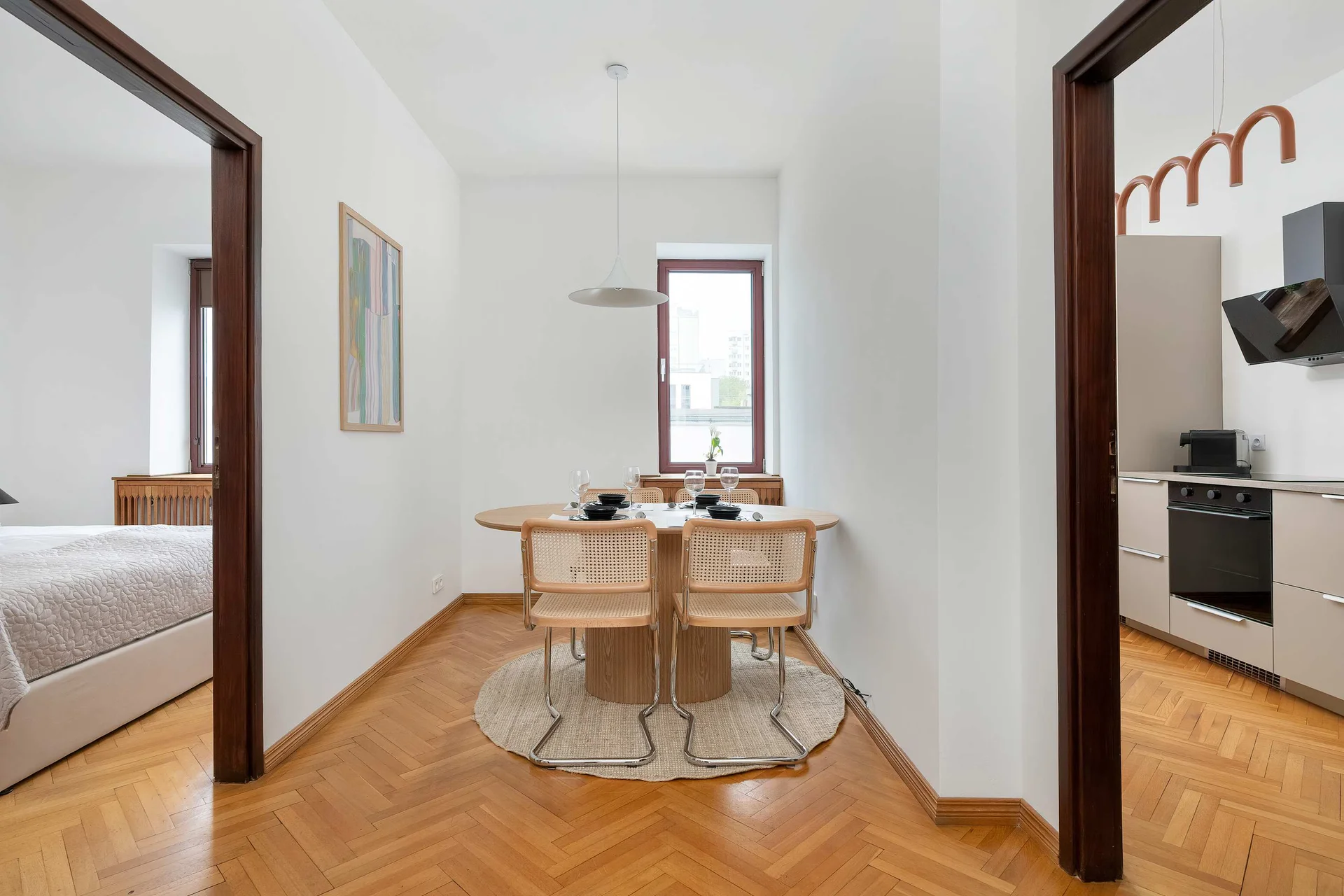 A dining area with a round table and modern chairs connects with the open apartment layout. The bright interior feels spacious and welcoming.