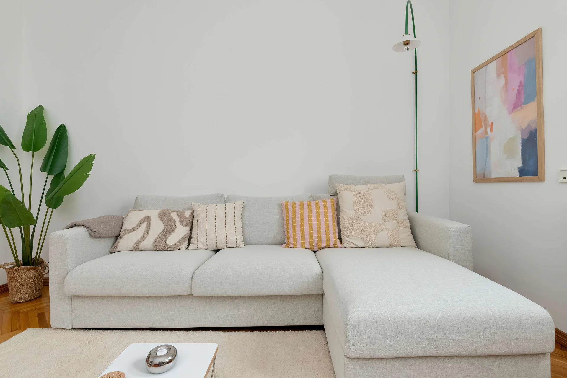 A cozy living room corner with a sectional sofa and decorative cushions creates a relaxing space. Light colors and simple décor add warmth to the interior.