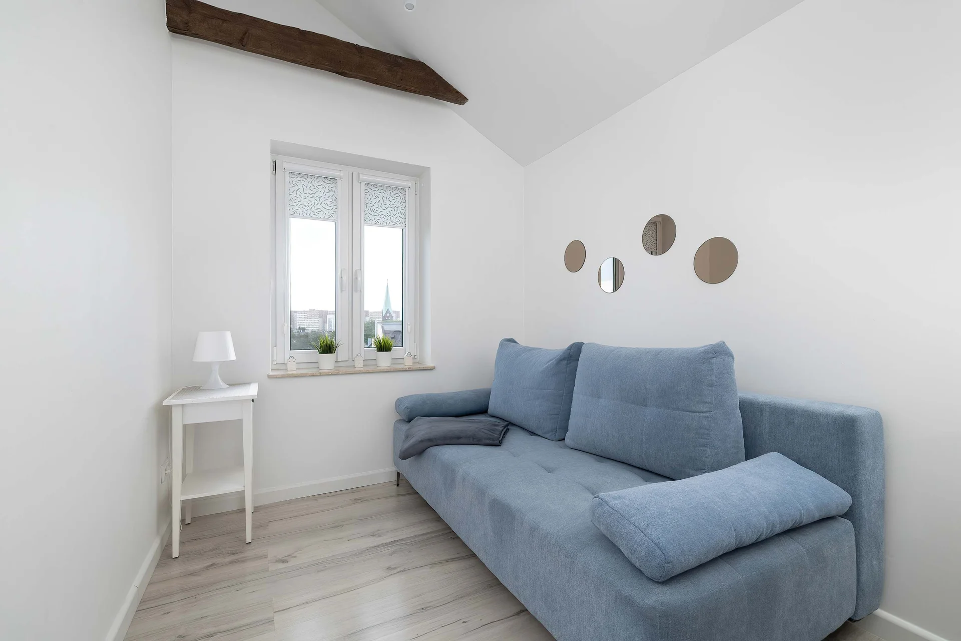 A cozy seating area with a blue sofa and a small dining table by the window. The room is bright and simply furnished.