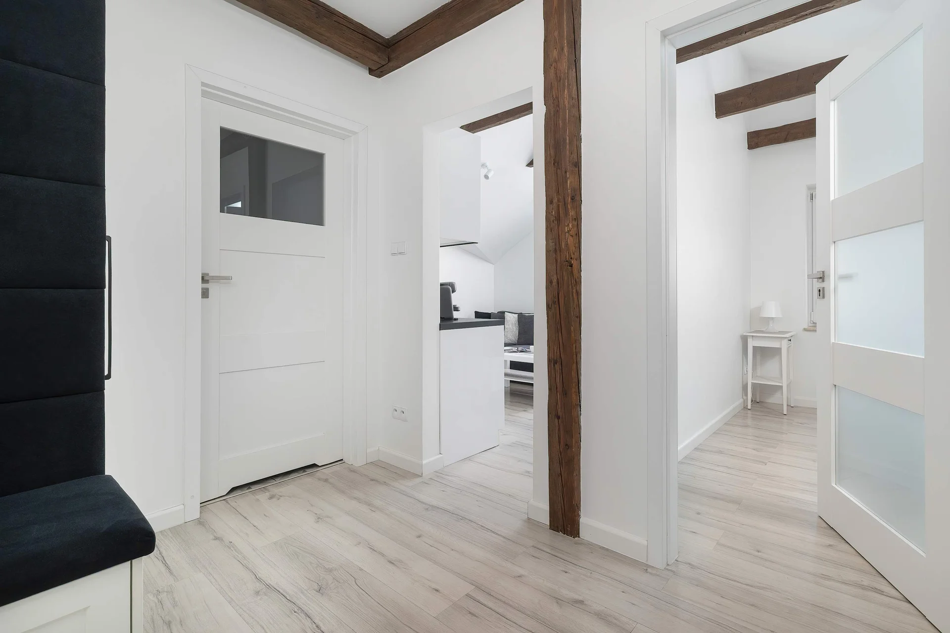 A modern entrance hall with light finishes and exposed wooden ceiling beams. The hallway provides access to the apartment's rooms.
