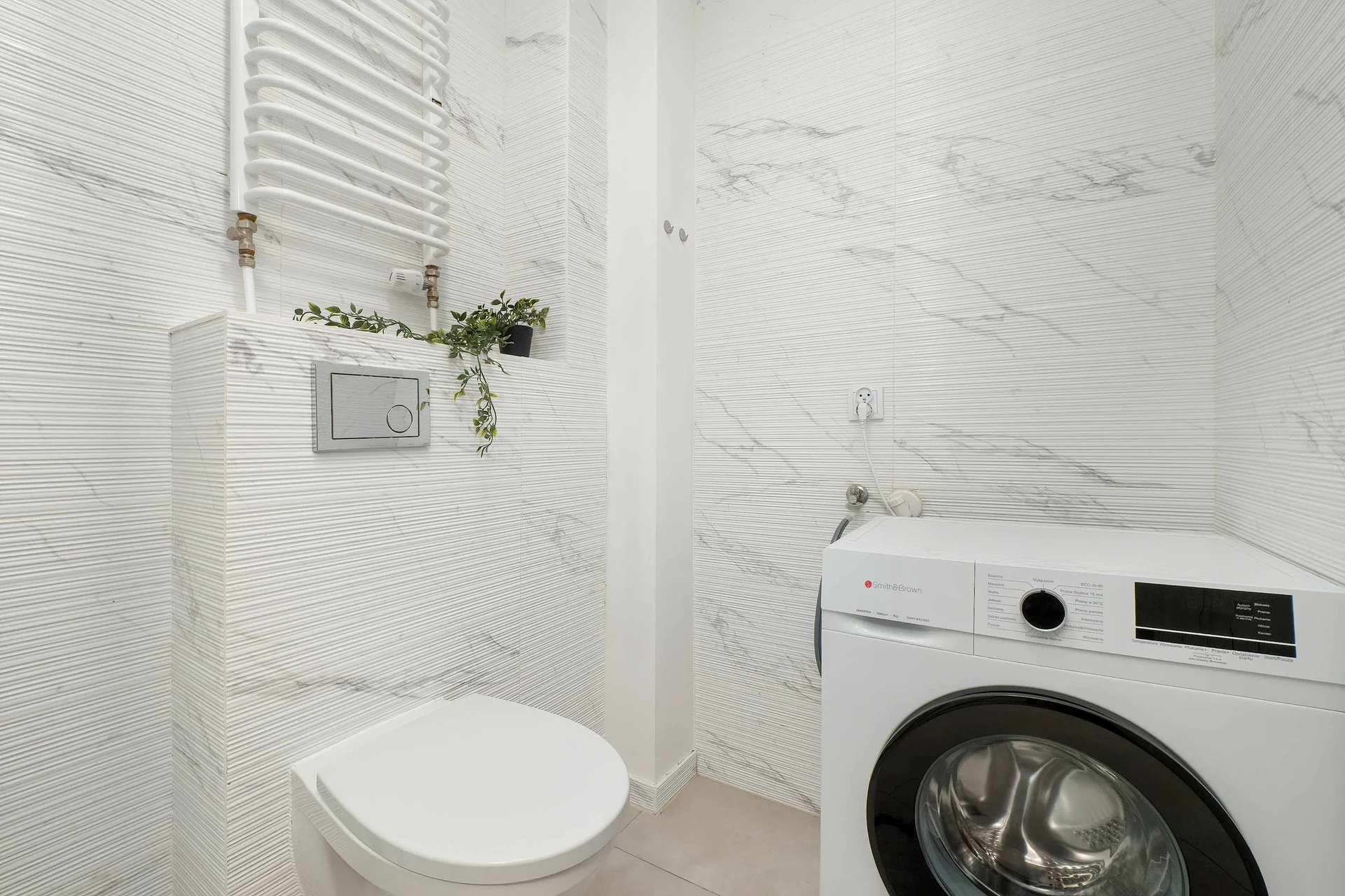 A modern bathroom with shower, toilet, and washing machine. Bright finishes give the room a clean and fresh look.