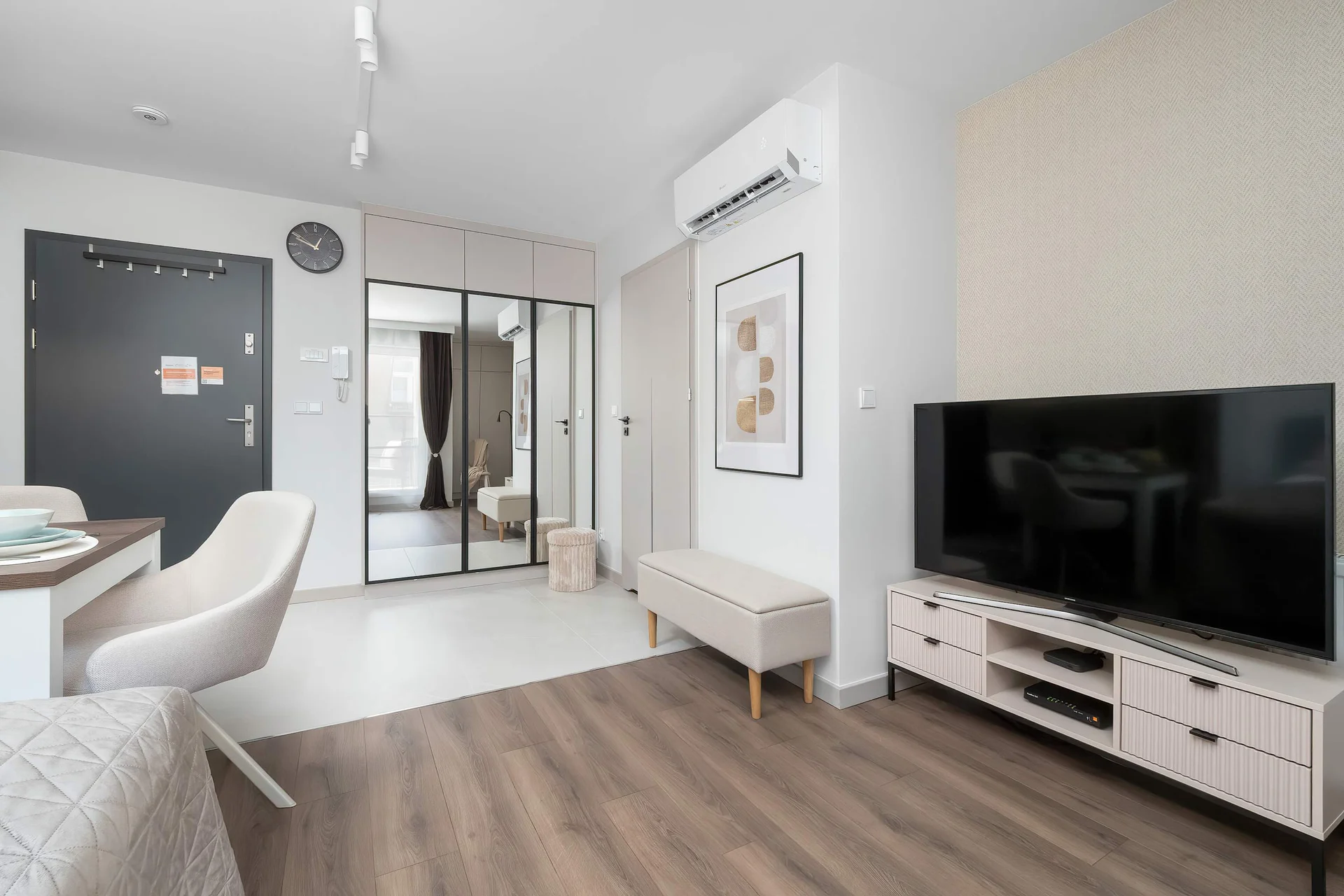 A view from the entryway showcases a spacious living room arrangement with a low-profile TV console. Recessed spotlights illuminate the clean wood-plank flooring that runs throughout the home.
