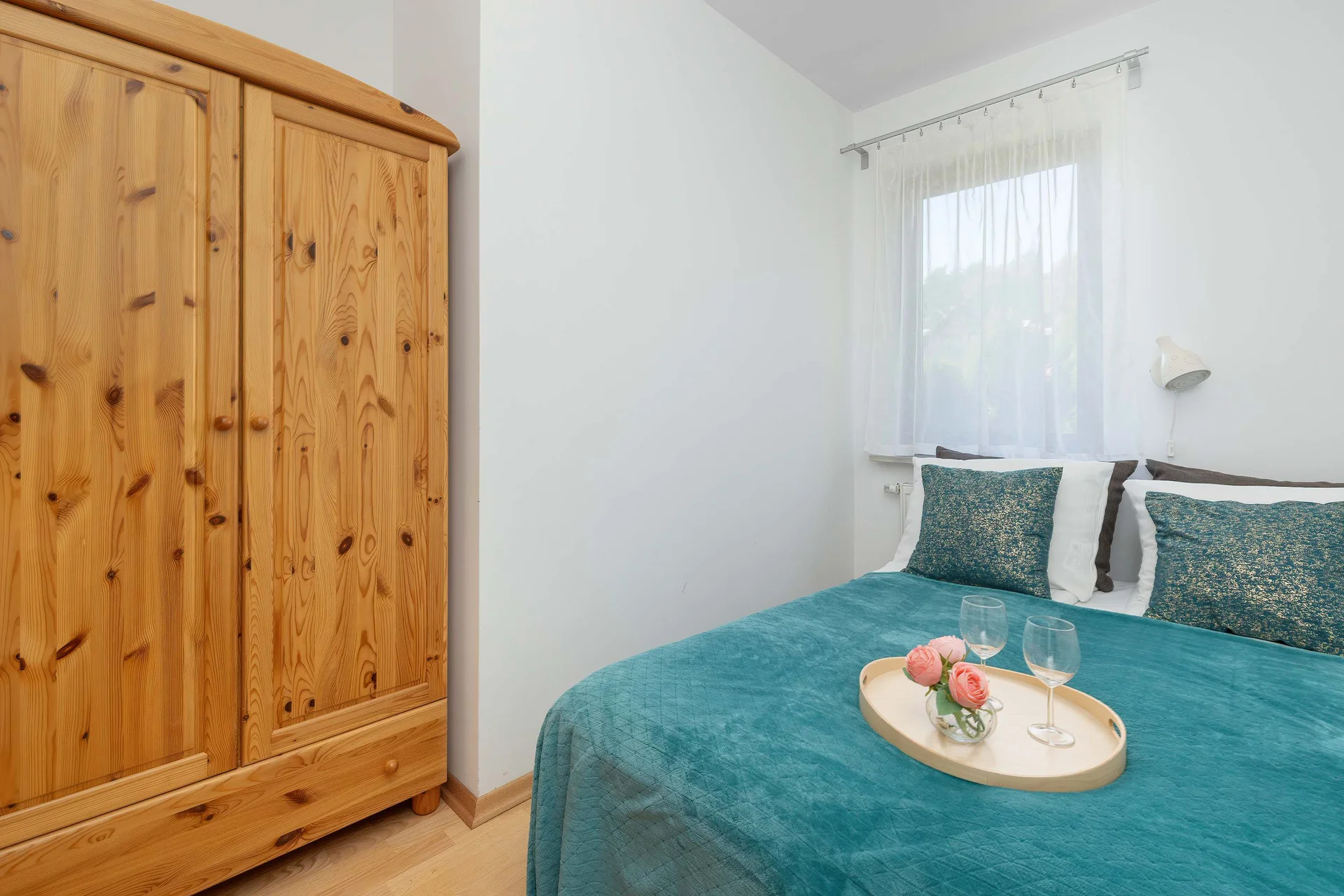 A bright bedroom with bed and a large wooden wardrobe. Simple décor creates a comfortable atmosphere.