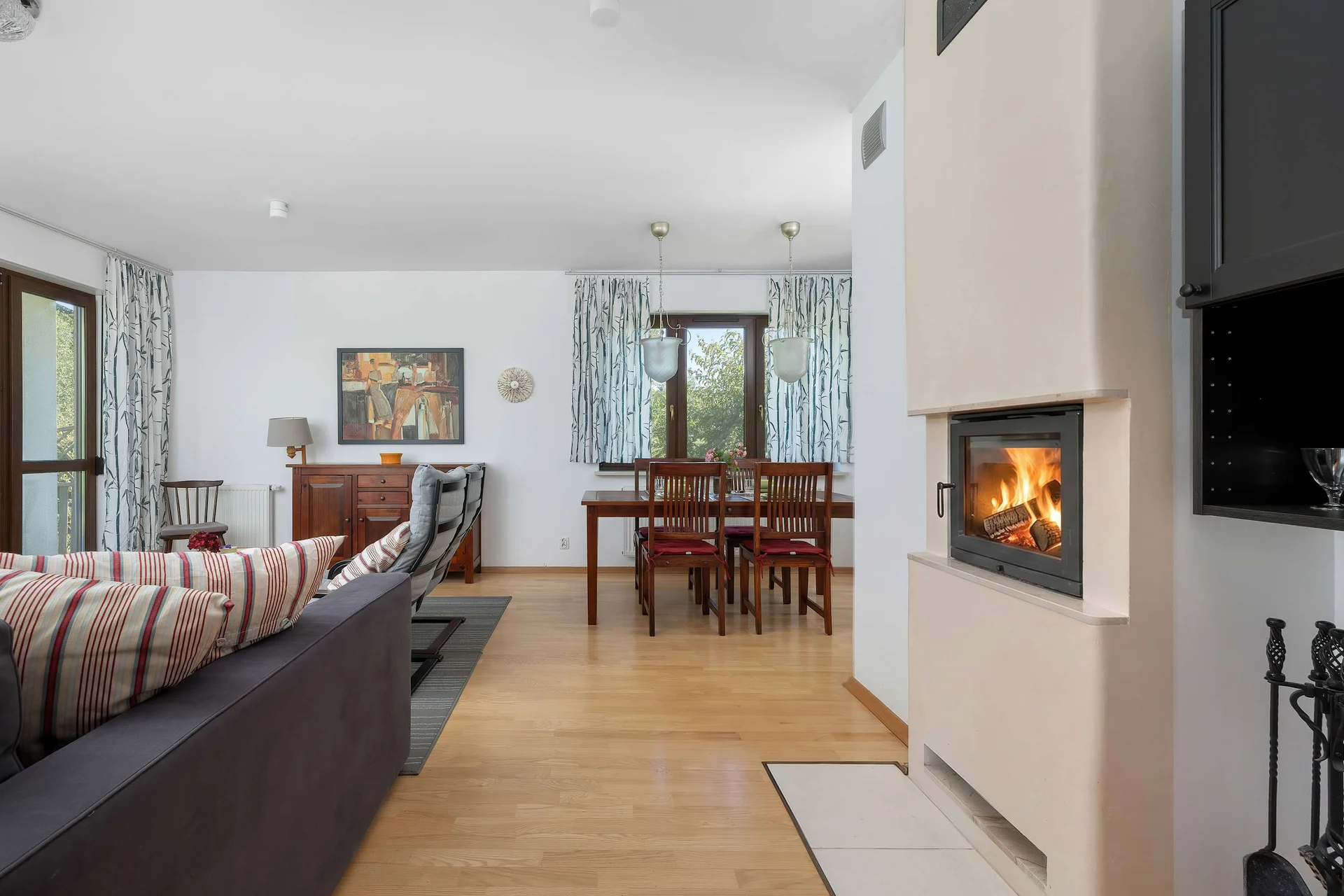 An open-plan living area with a sofa, dining table, and modern fireplace. The bright interior creates a warm and comfortable atmosphere.