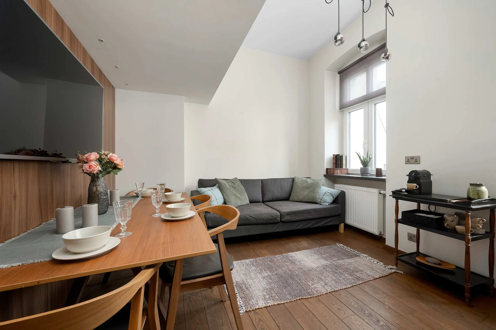 Bright and modern living room with a dining table, grey sofa, and large windows providing plenty of natural light.