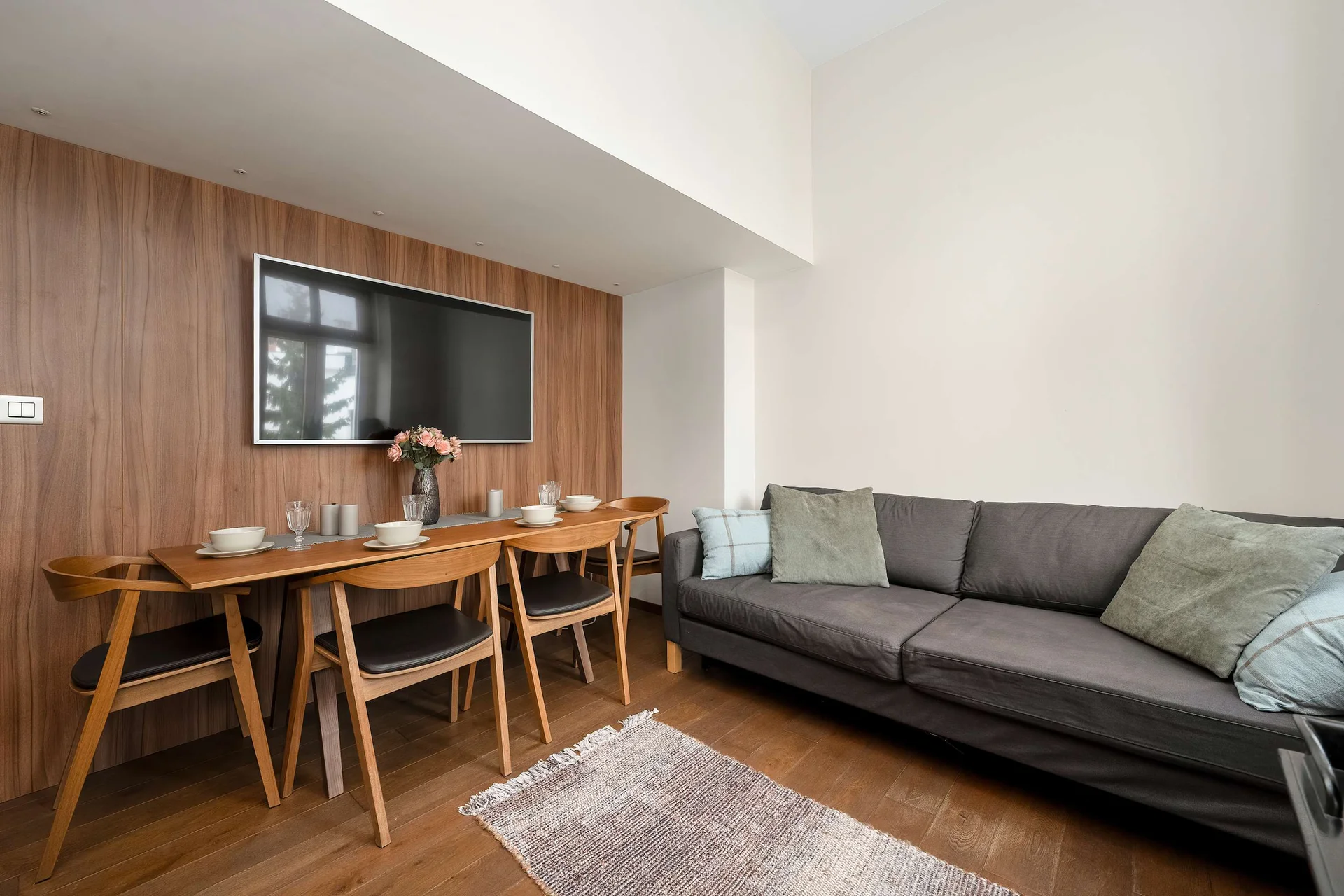 Spacious open-plan living area with a dining table, wooden cabinetry, and a comfortable sofa.