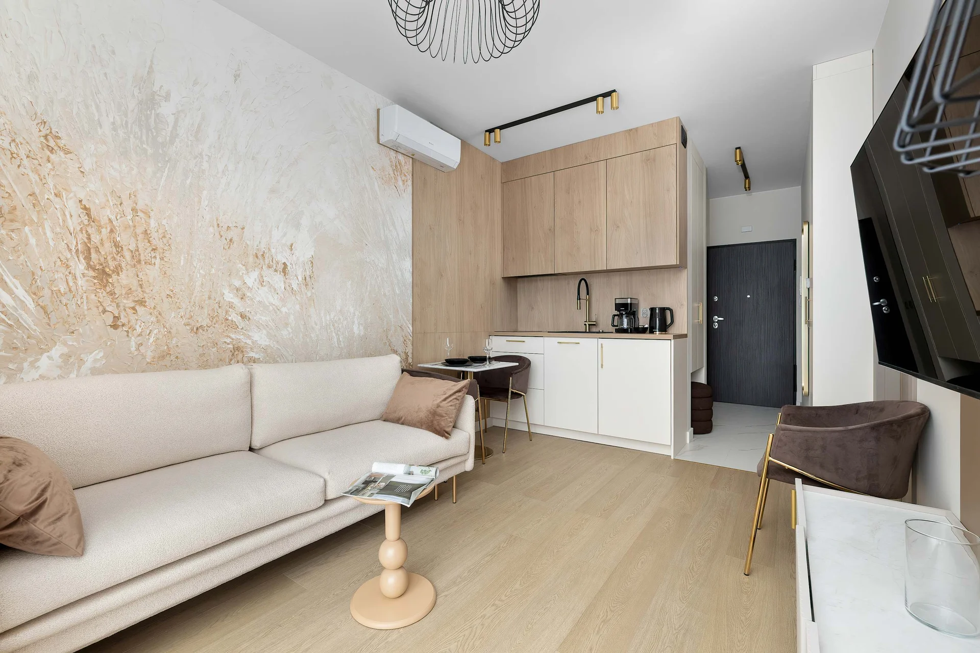 The living room is viewed from the opposite side, showcasing the sofa, TV, kitchenette, and decorative wall finishes. The compact design feels bright and welcoming.