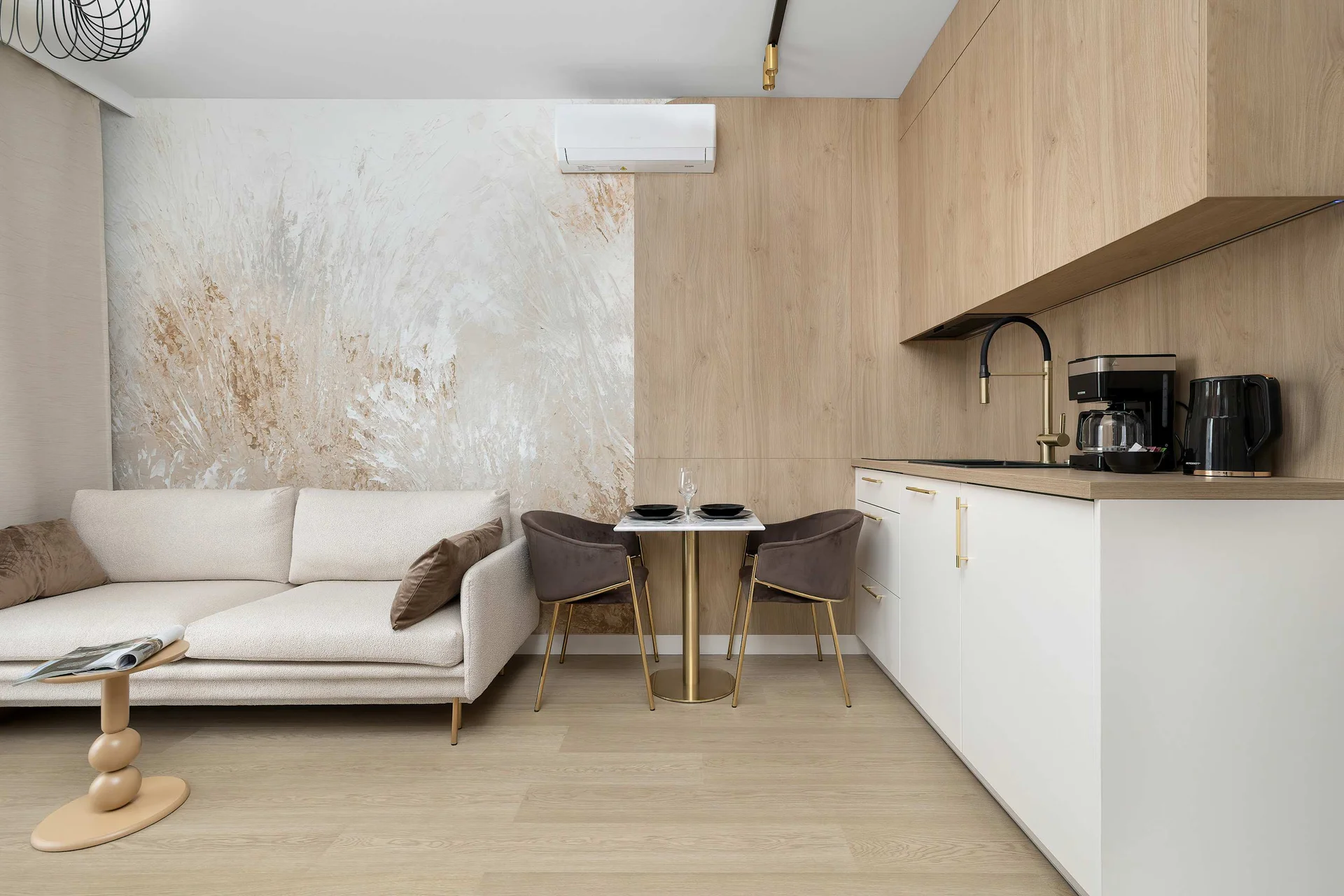 The open-plan living room combines a cozy seating area, kitchenette, and dining table in a bright contemporary space. Warm wood finishes complement the elegant interior.