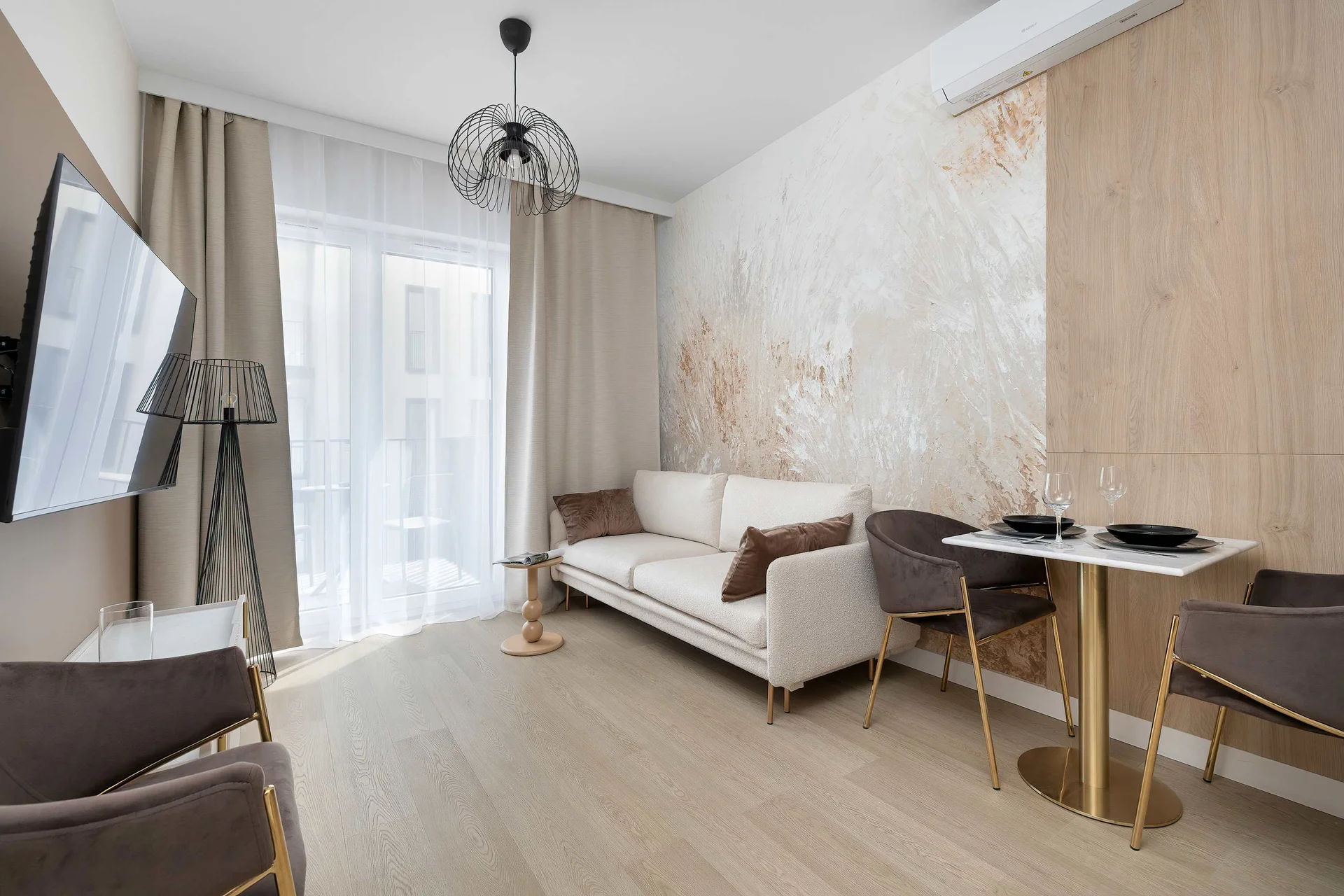 Another angle highlights the living area with a sofa, TV, kitchenette, and dining corner arranged in an efficient layout. Large windows bring natural light into the room.