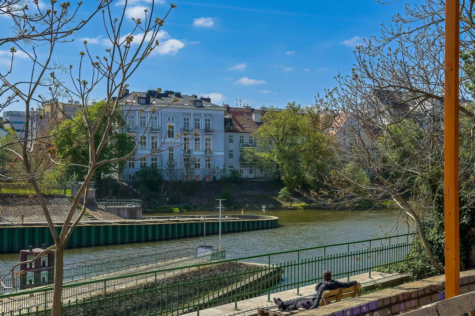 A scenic view of a canal, trees, and residential buildings. Large windows let in plenty of natural light.