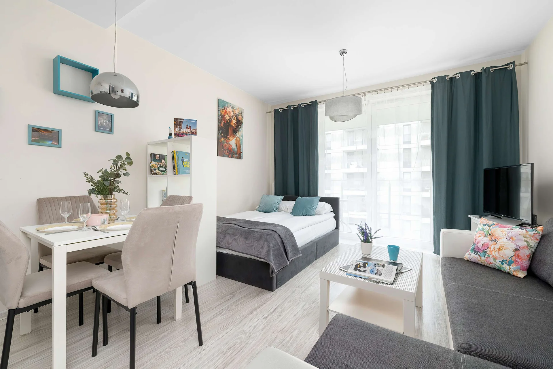 A bright and cozy living area with a comfortable sofa bed and a dining table. Large windows fill the apartment with natural light.