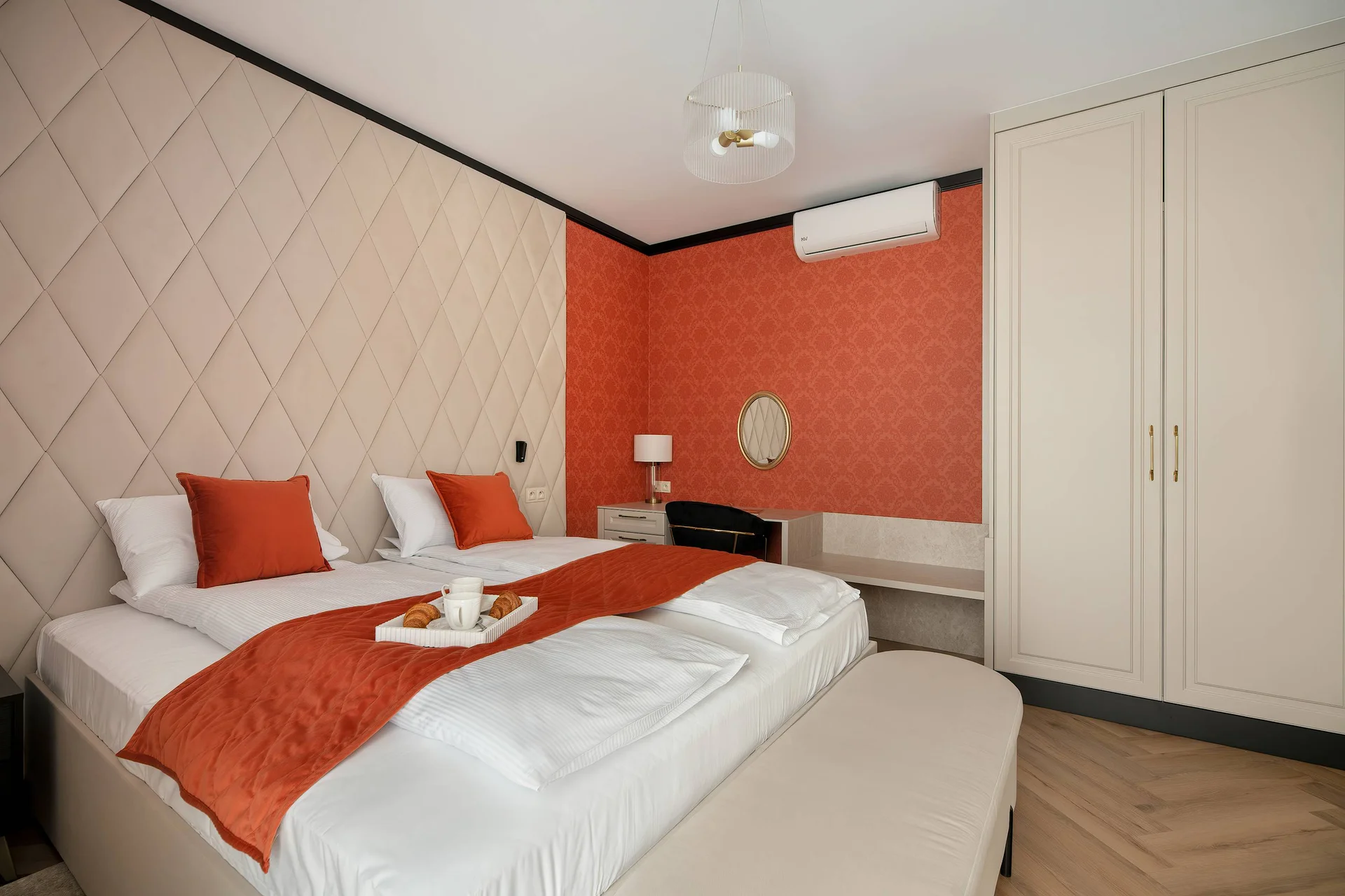 A cozy bedroom with a double bed styled with orange accents and a white padded headboard. Large built-in wardrobes sit on the side, creating a clean aesthetic.