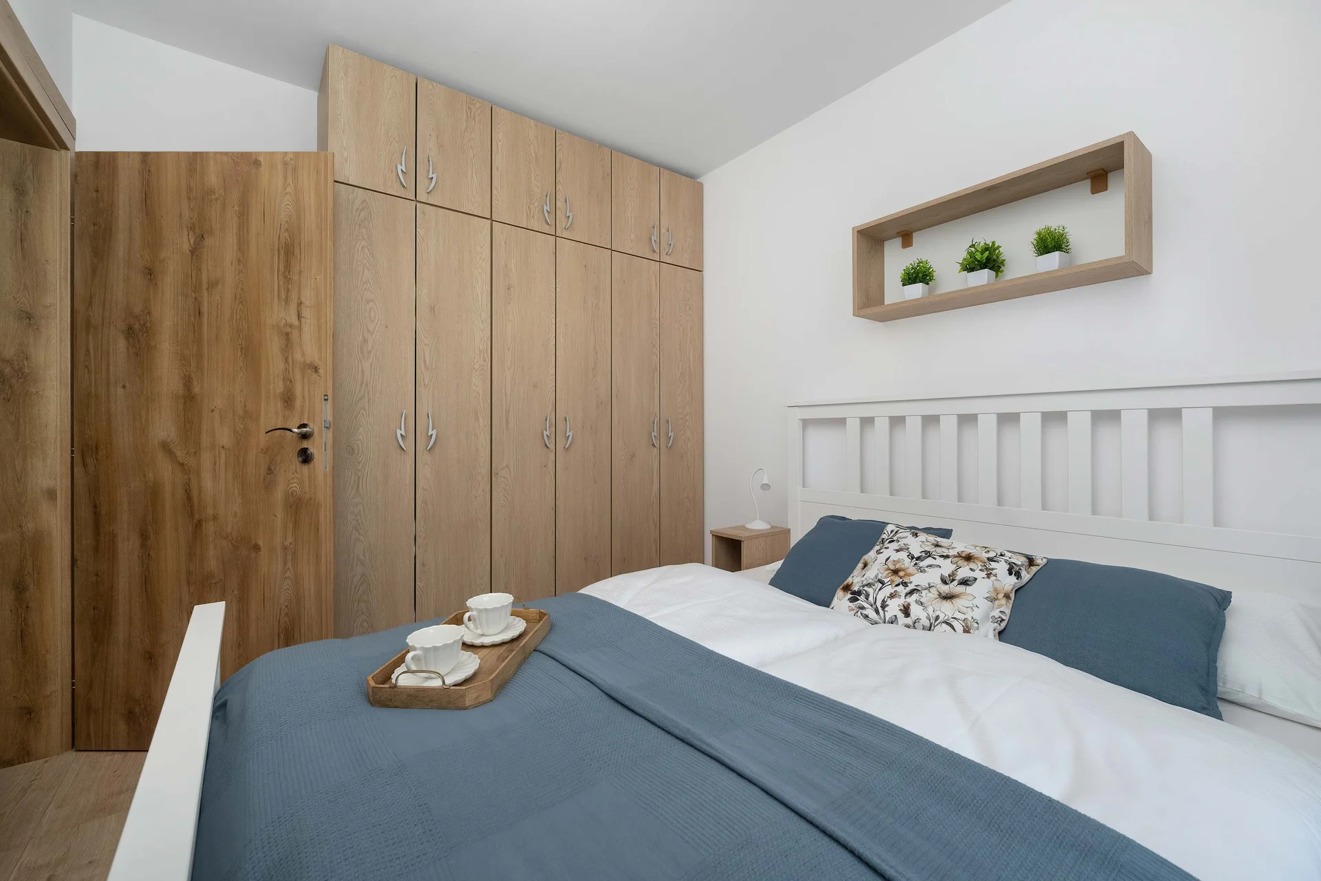 A bright bedroom offers a large double bed. A spacious wooden wardrobe provides ample storage right next to the sleeping area.