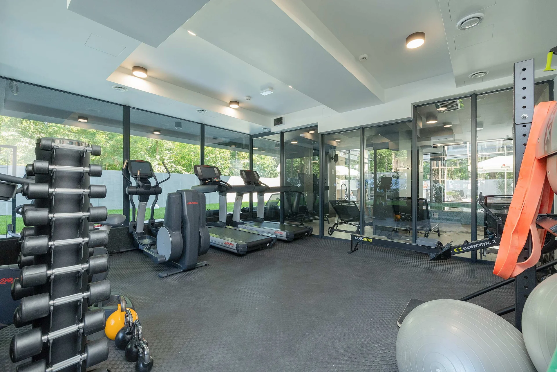 Modern fitness room with large windows, various exercise machines, weights and gym equipment in a spacious interior.