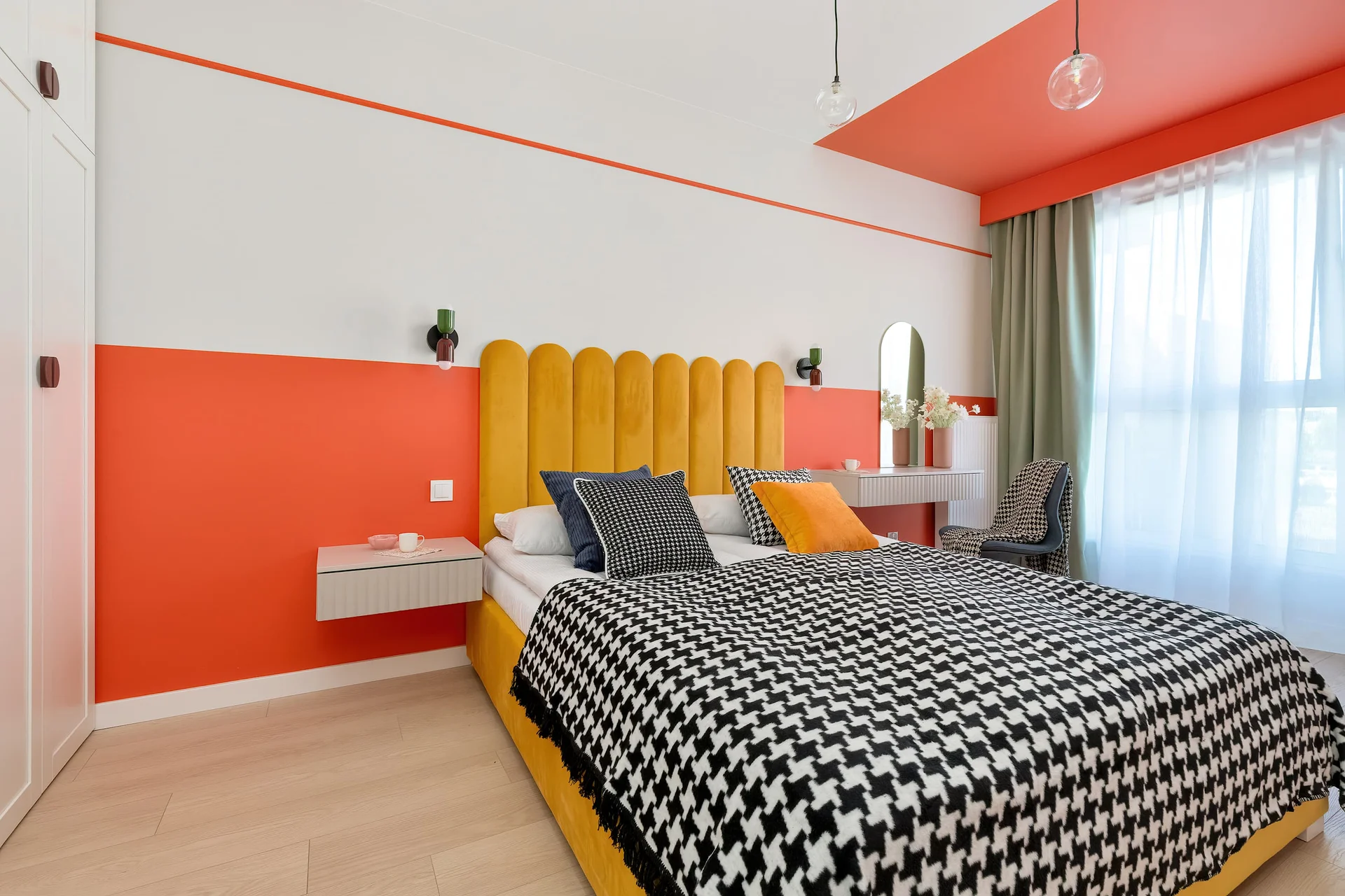 A modern bedroom with a double bed, checkered bedding, and a bold orange accent wall.