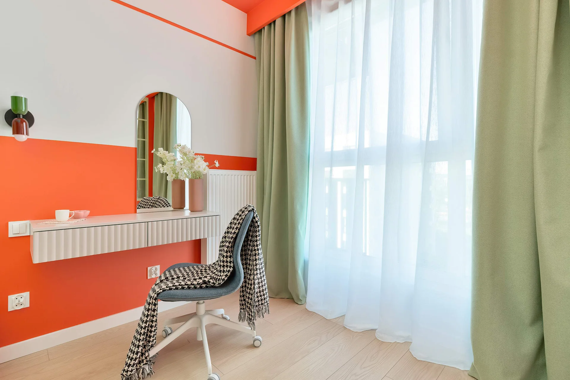 A cozy desk area with a chair, orange desk, and large window with sheer curtains.